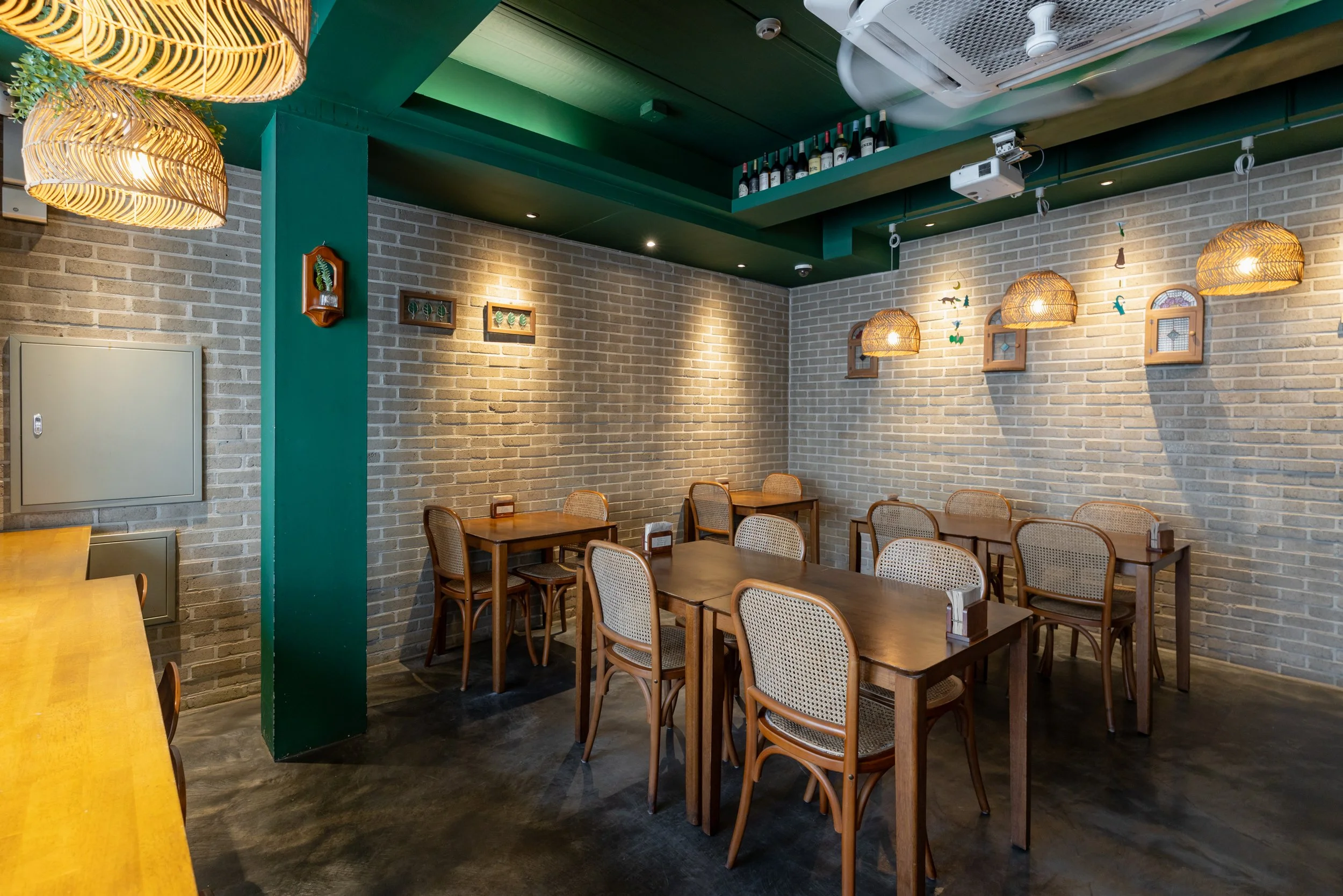 Empty restaurant with wooden tables and chairs, brick walls, hanging wicker lamps, and decorative wall hangings.