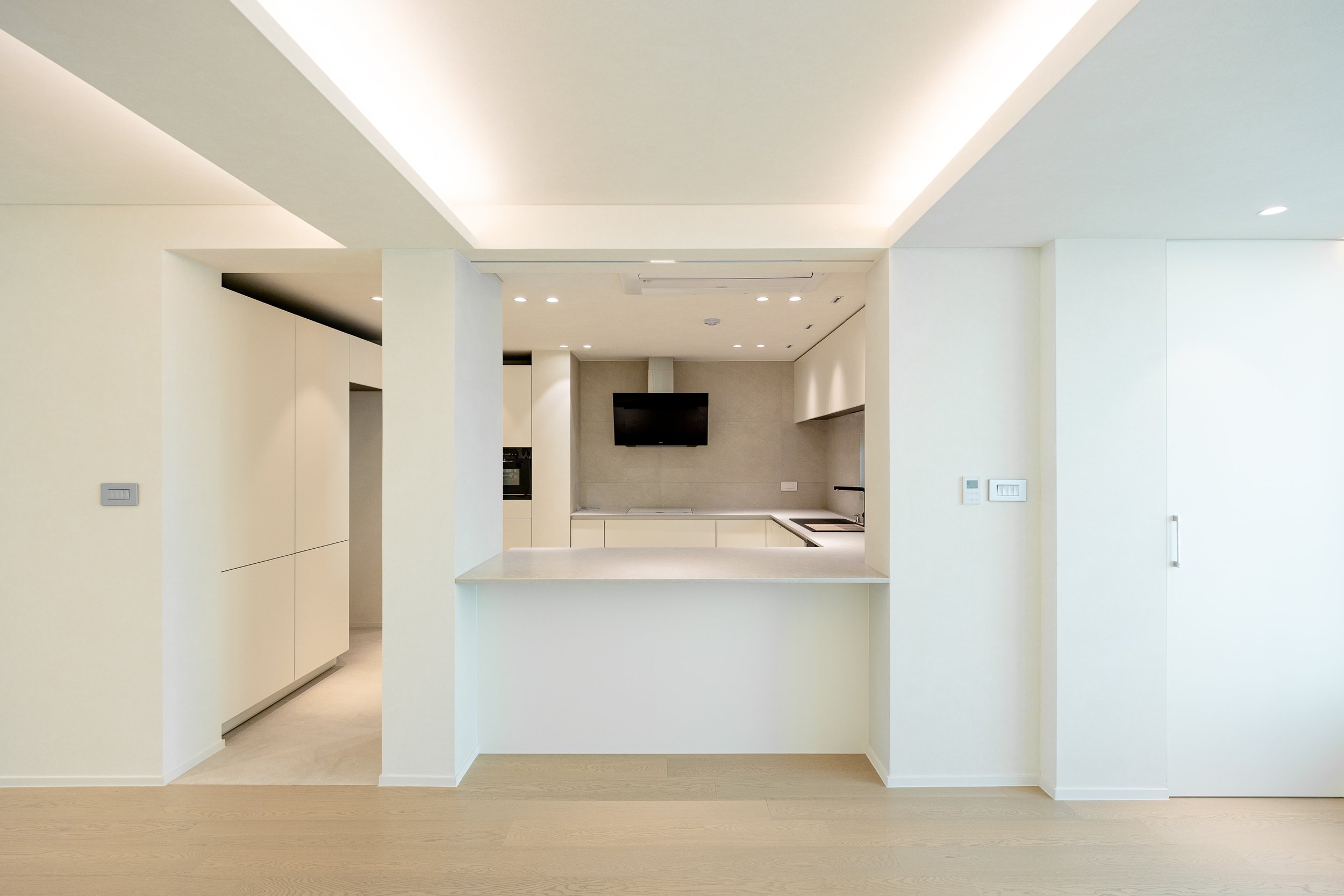 Empty modern kitchen with white cabinets, a central island, a wall-mounted television, and integrated appliances.