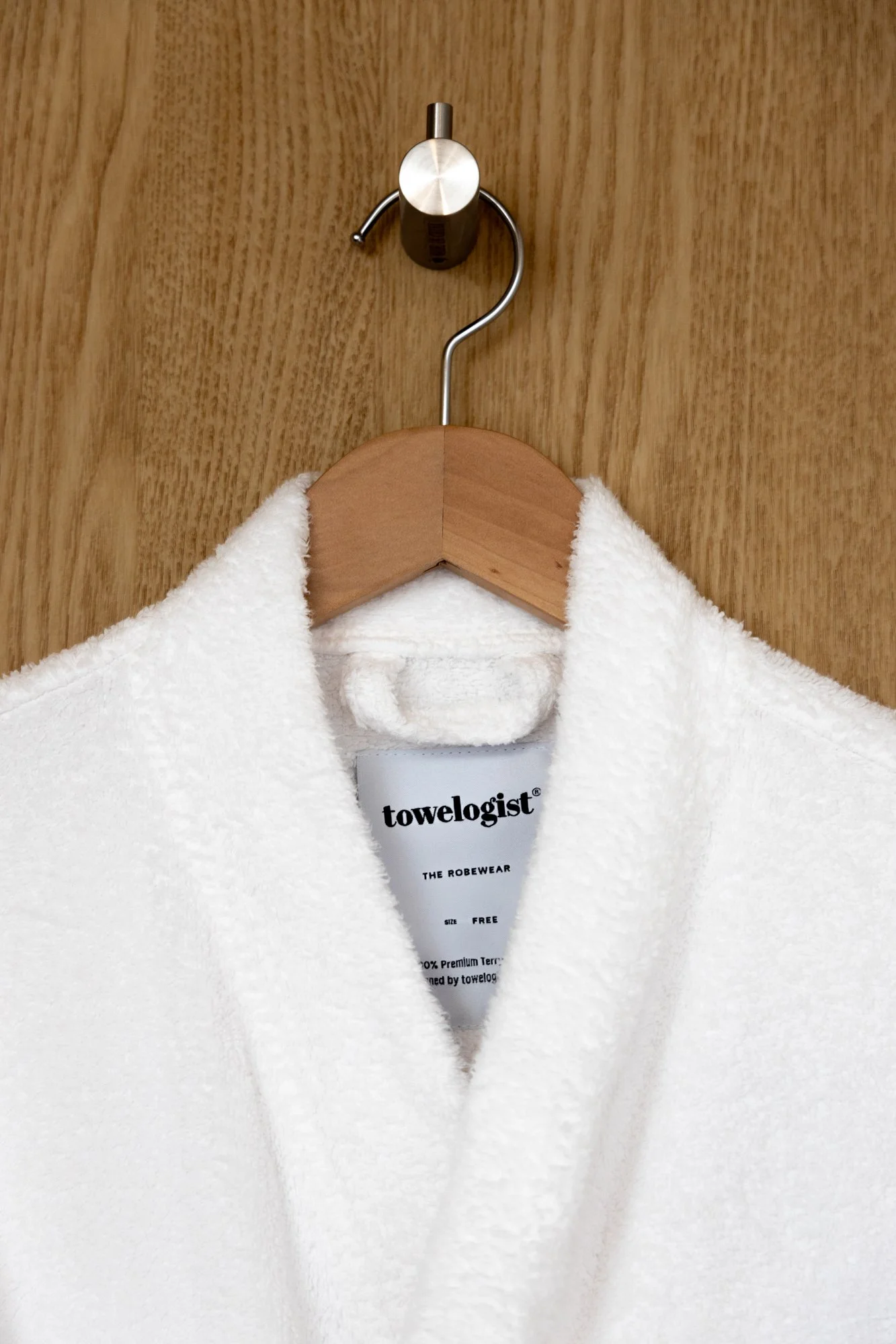 White towel hanging on a wooden hanger on a wooden wall with a towelologist brand label.