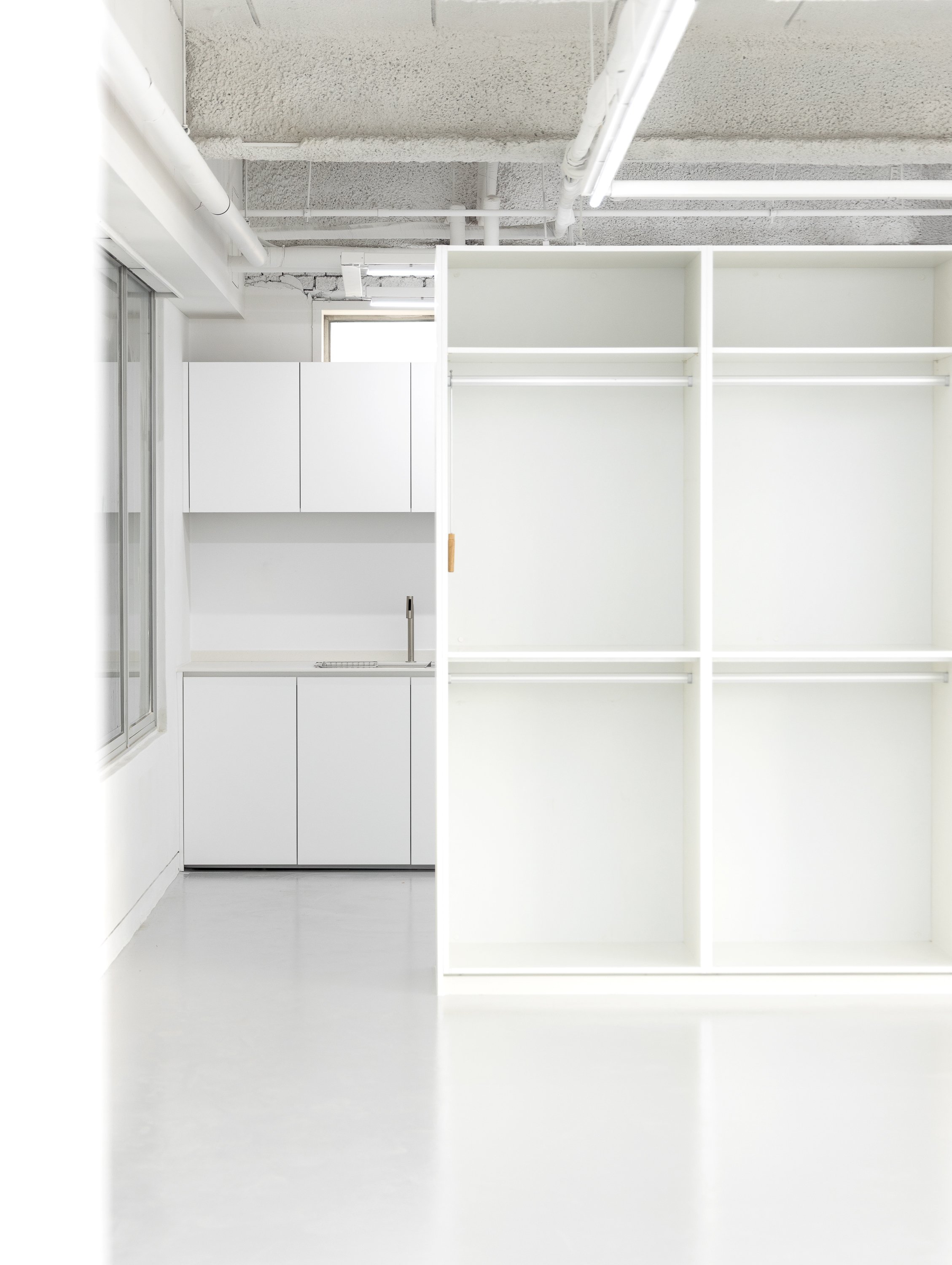 Empty white closet with shelves and hanging rods in a bright room with a window.
