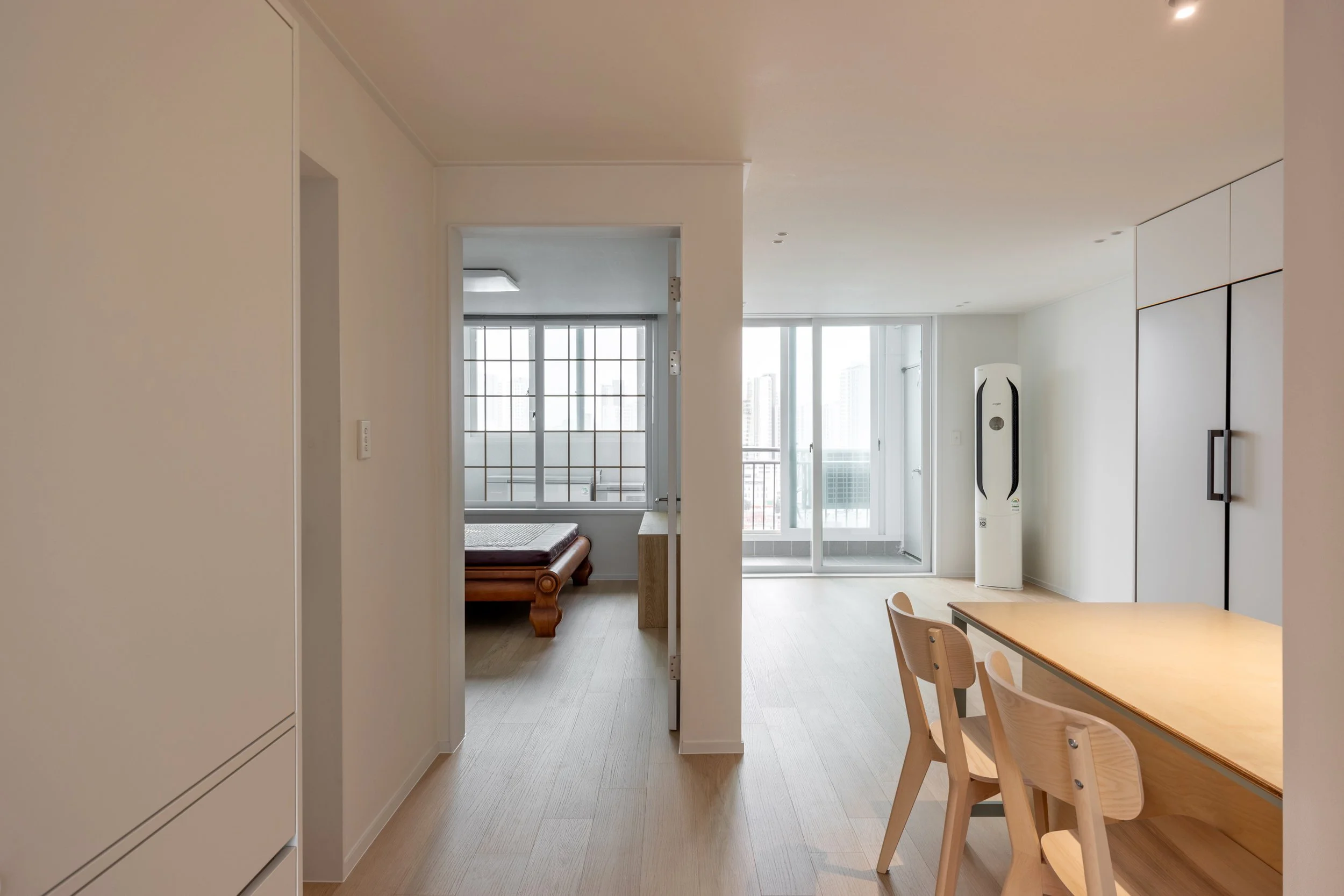 Interior of a modern apartment with a dining table, chairs, a standing air purifier, and a balcony door with city views.