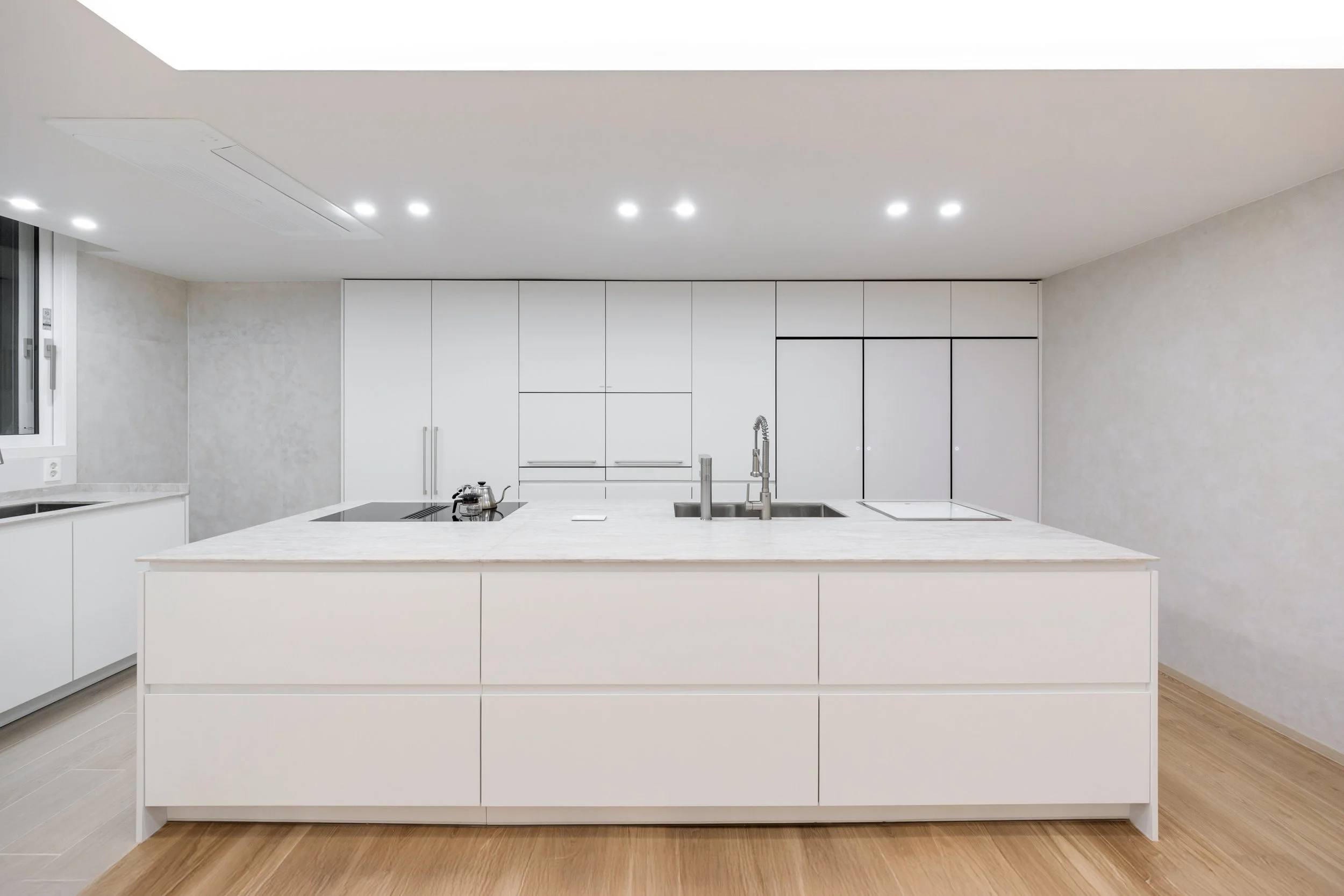 Modern, minimalist white kitchen with island, built-in appliances, and light wood flooring.