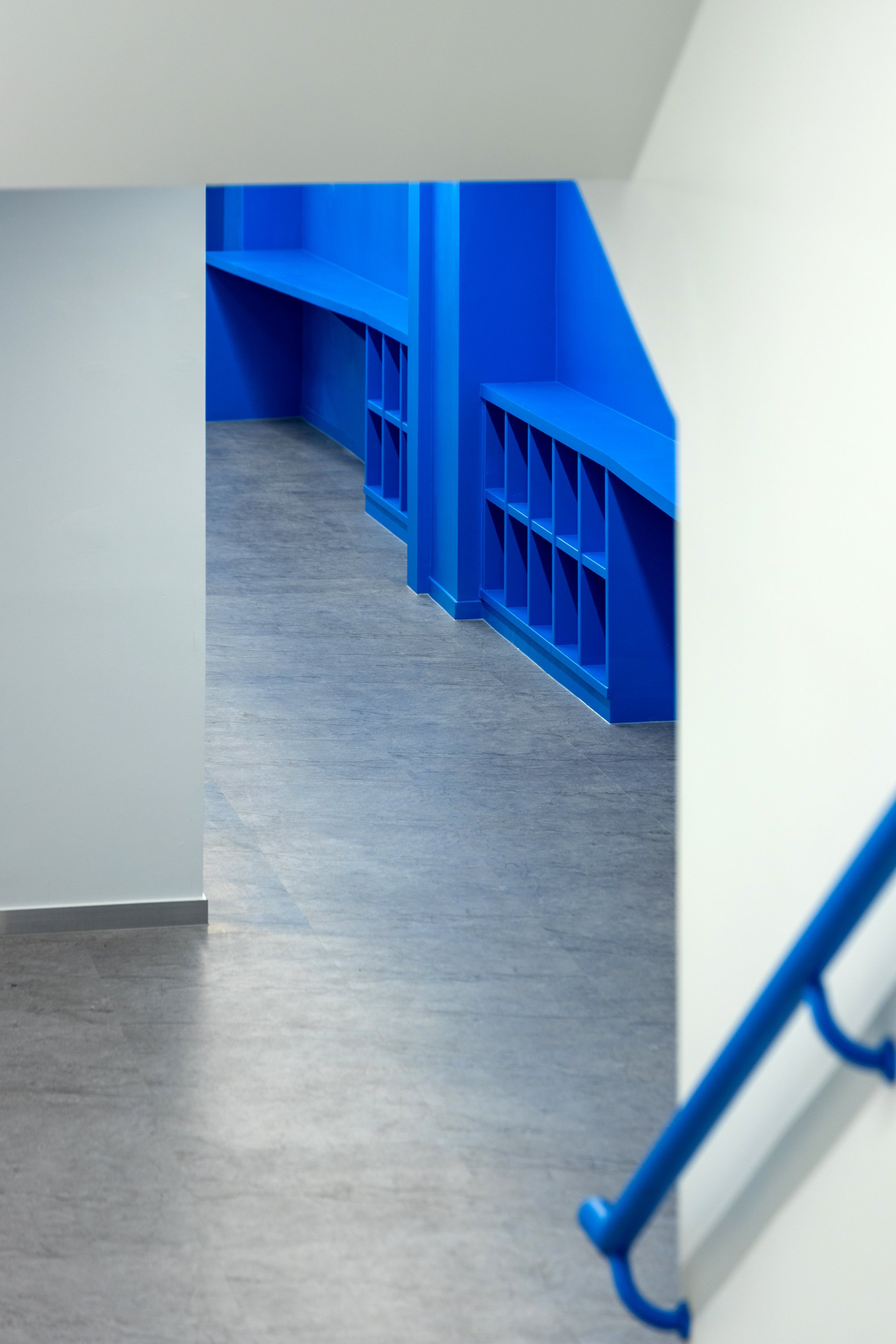Blue built-in shelving and storage unit in a modern room with gray flooring, framed by white walls and an architectural opening.