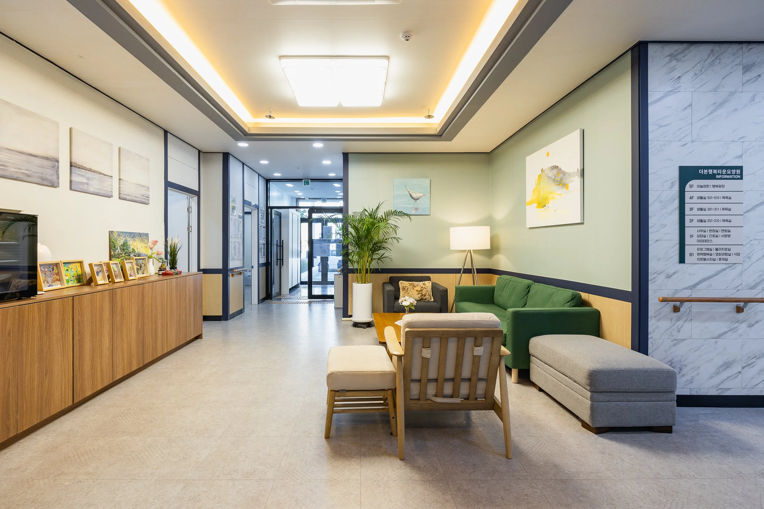 Lobby with a green sofa, armchair, lamps, artwork, and a wooden console table with framed pictures and decorations.