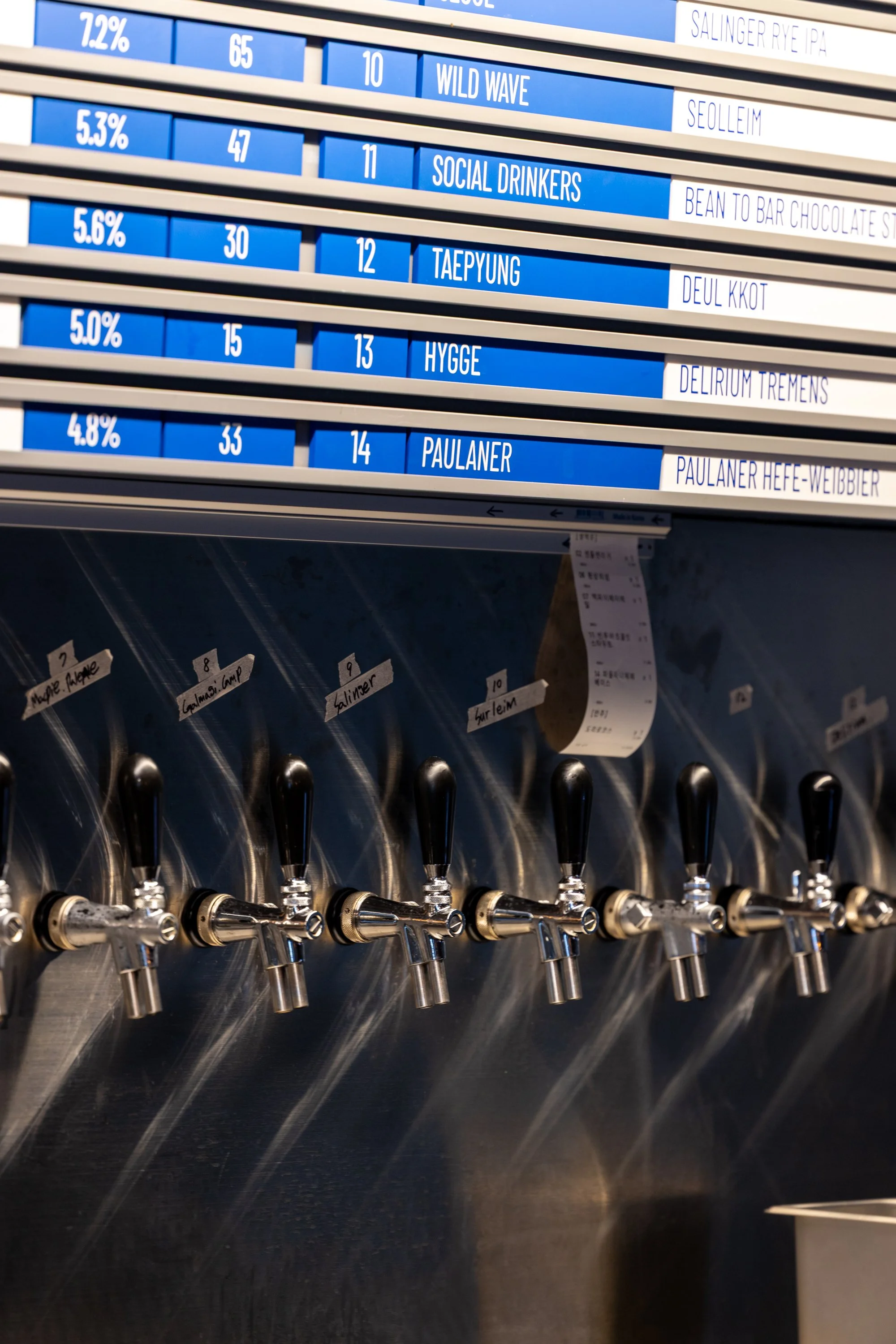 A row of beer taps with a digital beer menu above listing various beers, their alcohol percentages, and names.