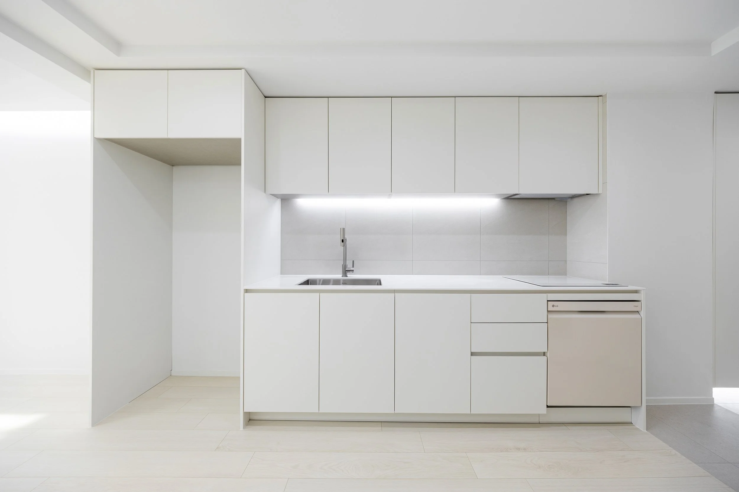 Minimalist white kitchen with cabinets, a stainless steel sink, and an electric stove, illuminated by under-cabinet lighting.