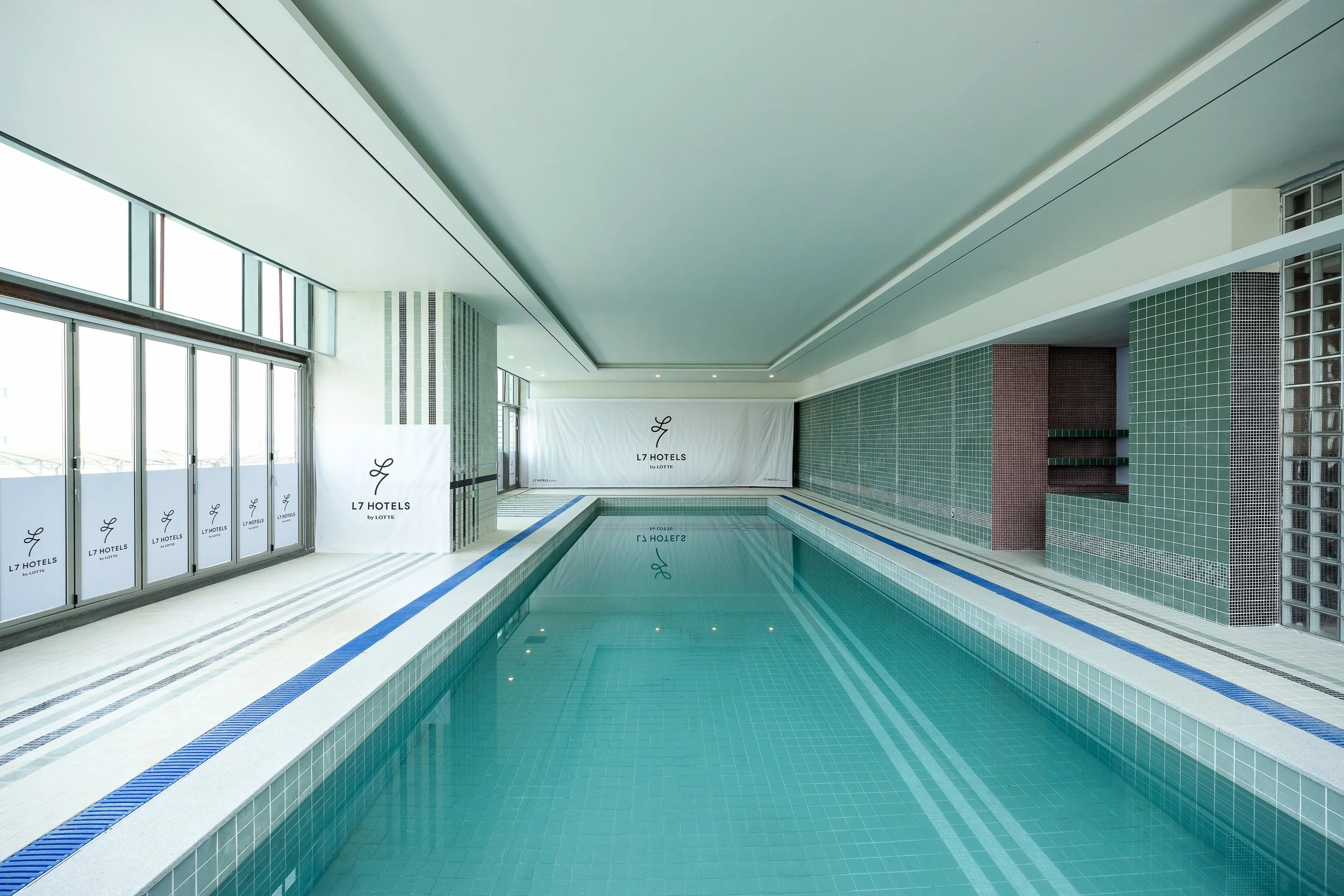 Indoor swimming pool at L7 Hotels with large windows and tiled walls