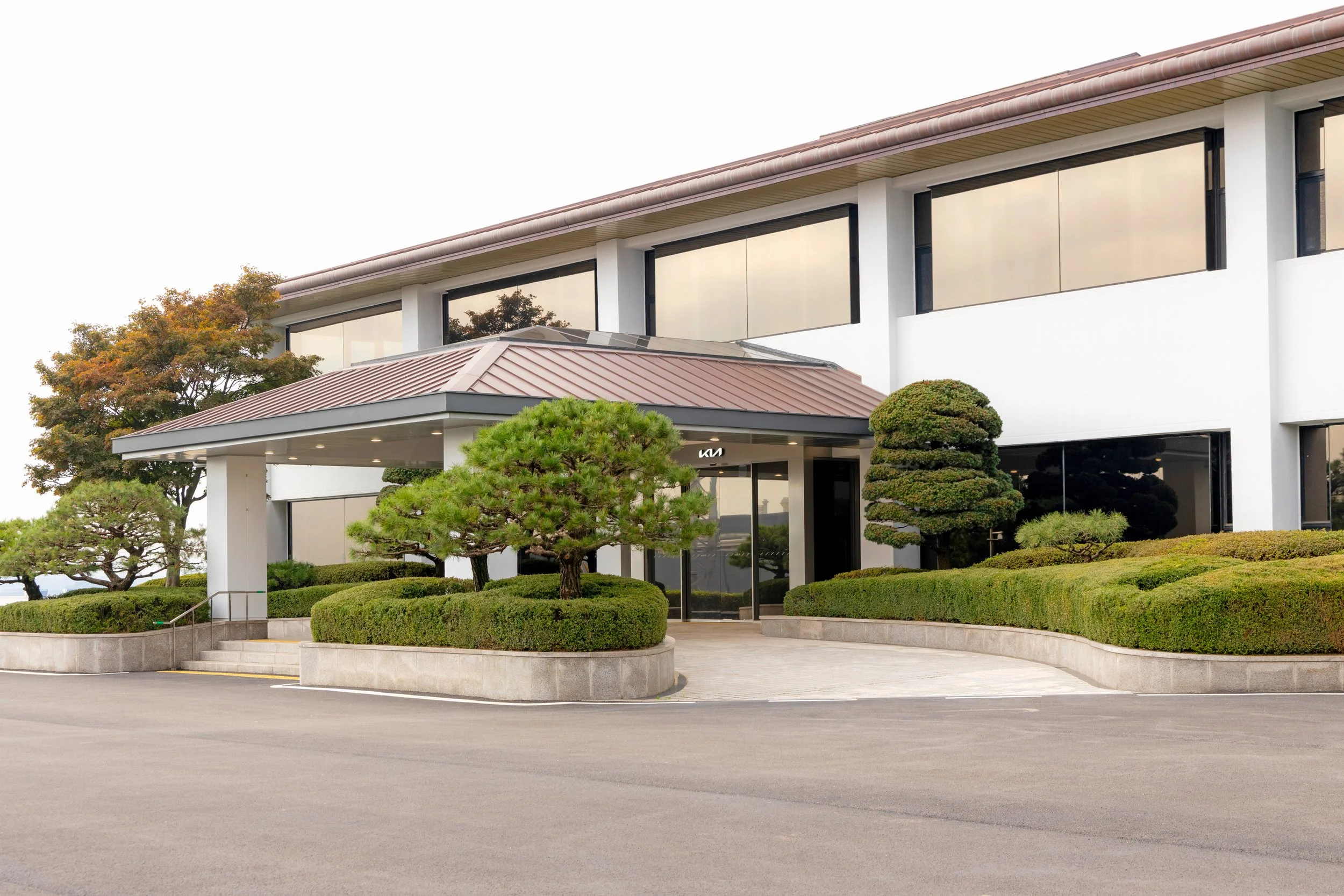 Modern commercial building with a landscaped entrance featuring trimmed bushes and trees