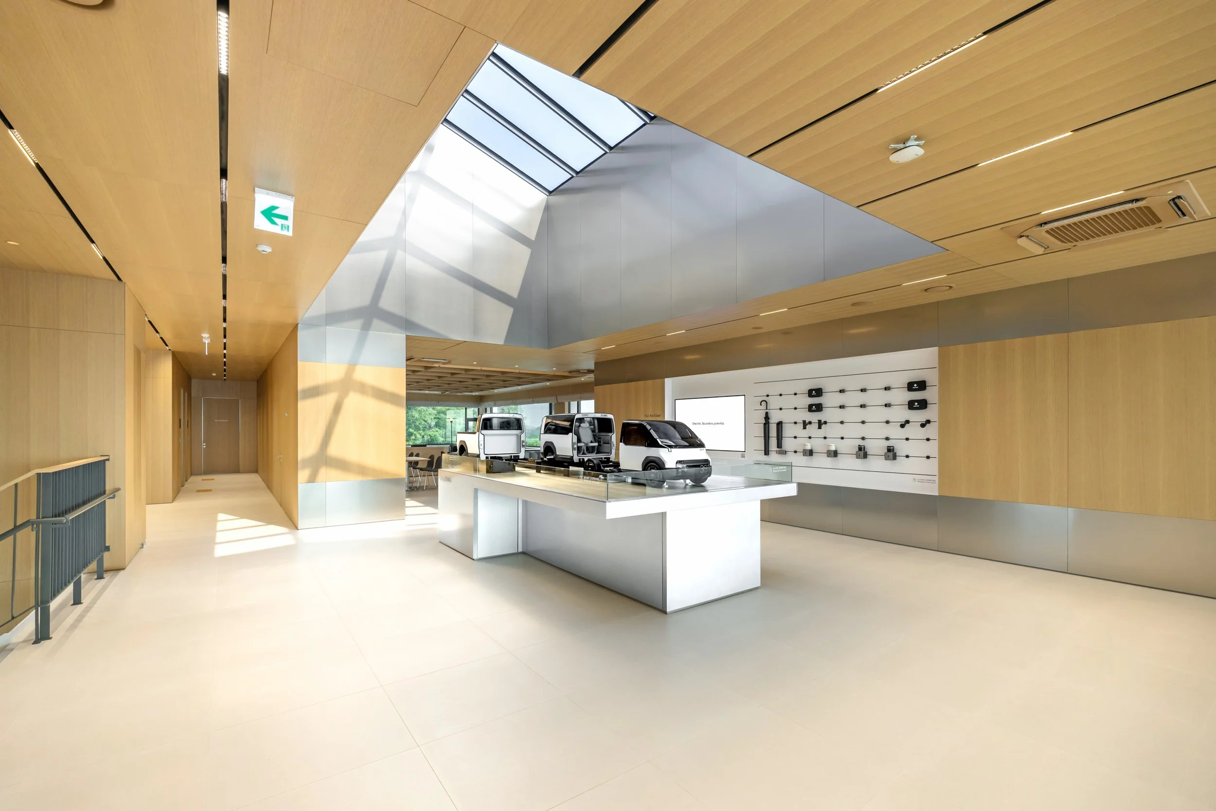 Modern interior space with light wood and metallic walls, a skylight, cars on display on a white table, and a pegboard with tools on the wall.