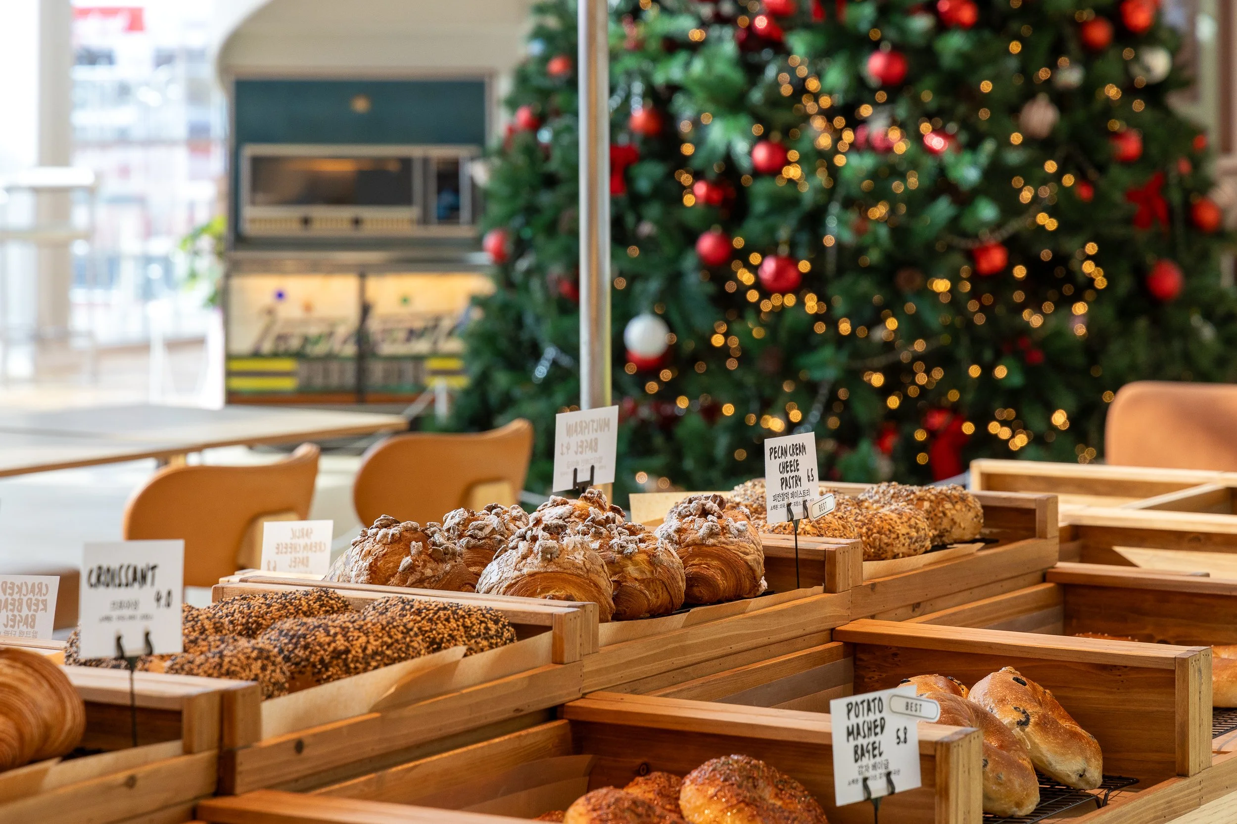 Assorted baked goods including croissants and muffins on display at a bakery with a Christmas tree in the background.