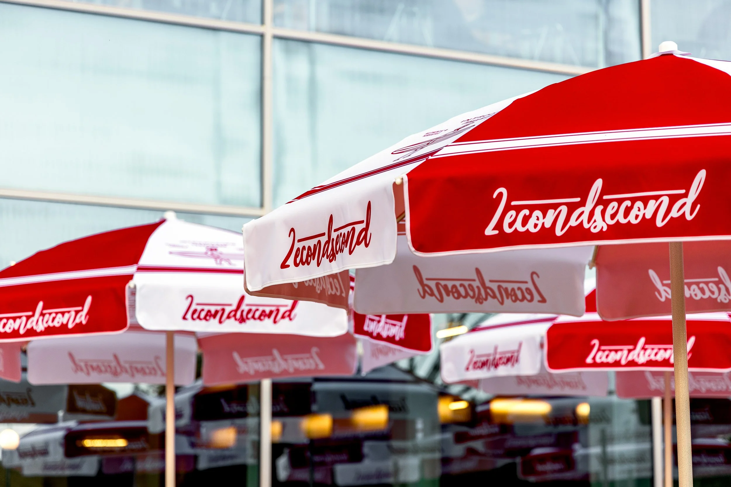 Red and white umbrellas with the text '2seconds' printed on them, set outdoors in front of a modern glass building.