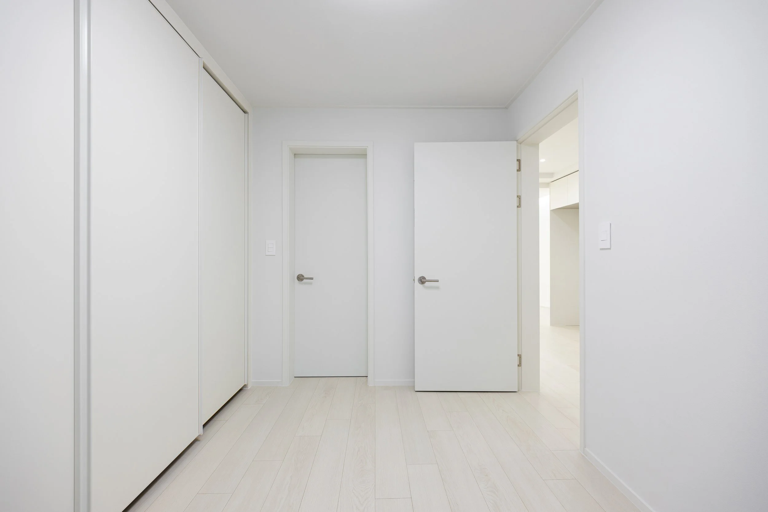 Empty white room with closed closet doors on the left and two open doors in the center, leading to other rooms.