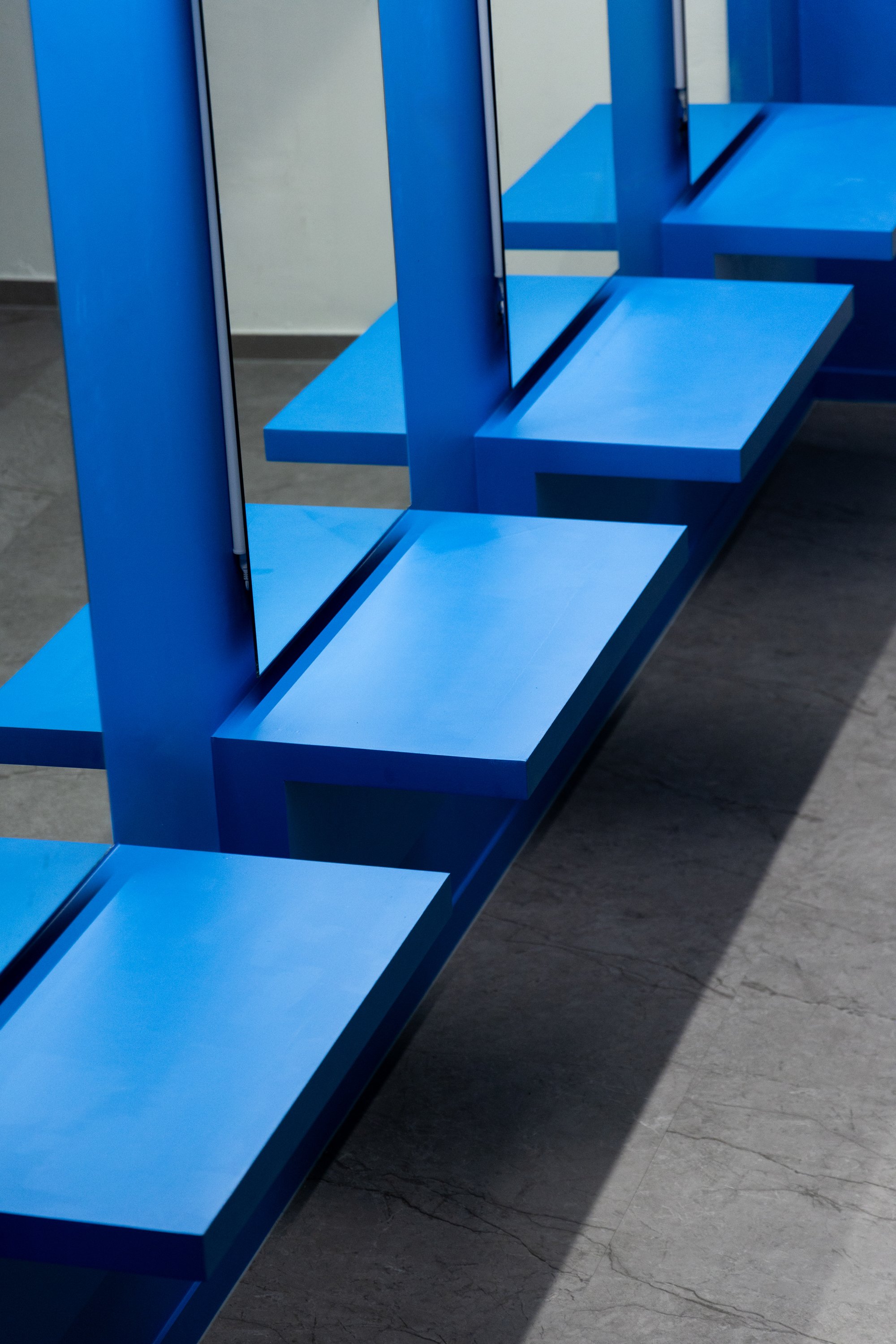Empty blue benches with angled seats and mirrors in a modern interior setting.