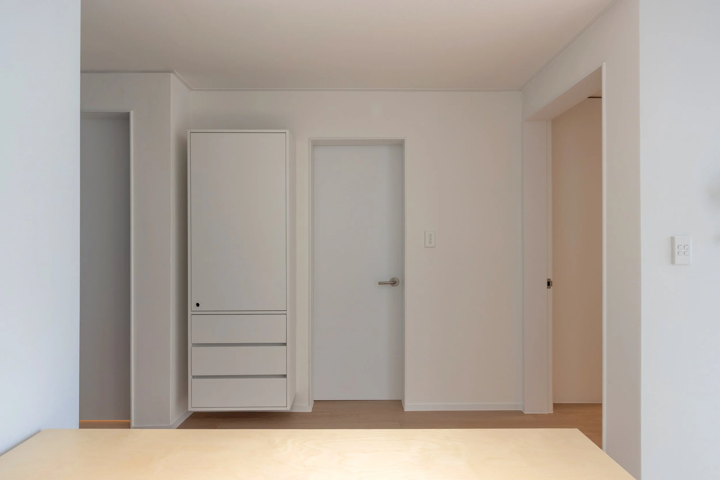 White wall with closed door, built-in cabinet, and doorway in a minimalist room with wooden floor.