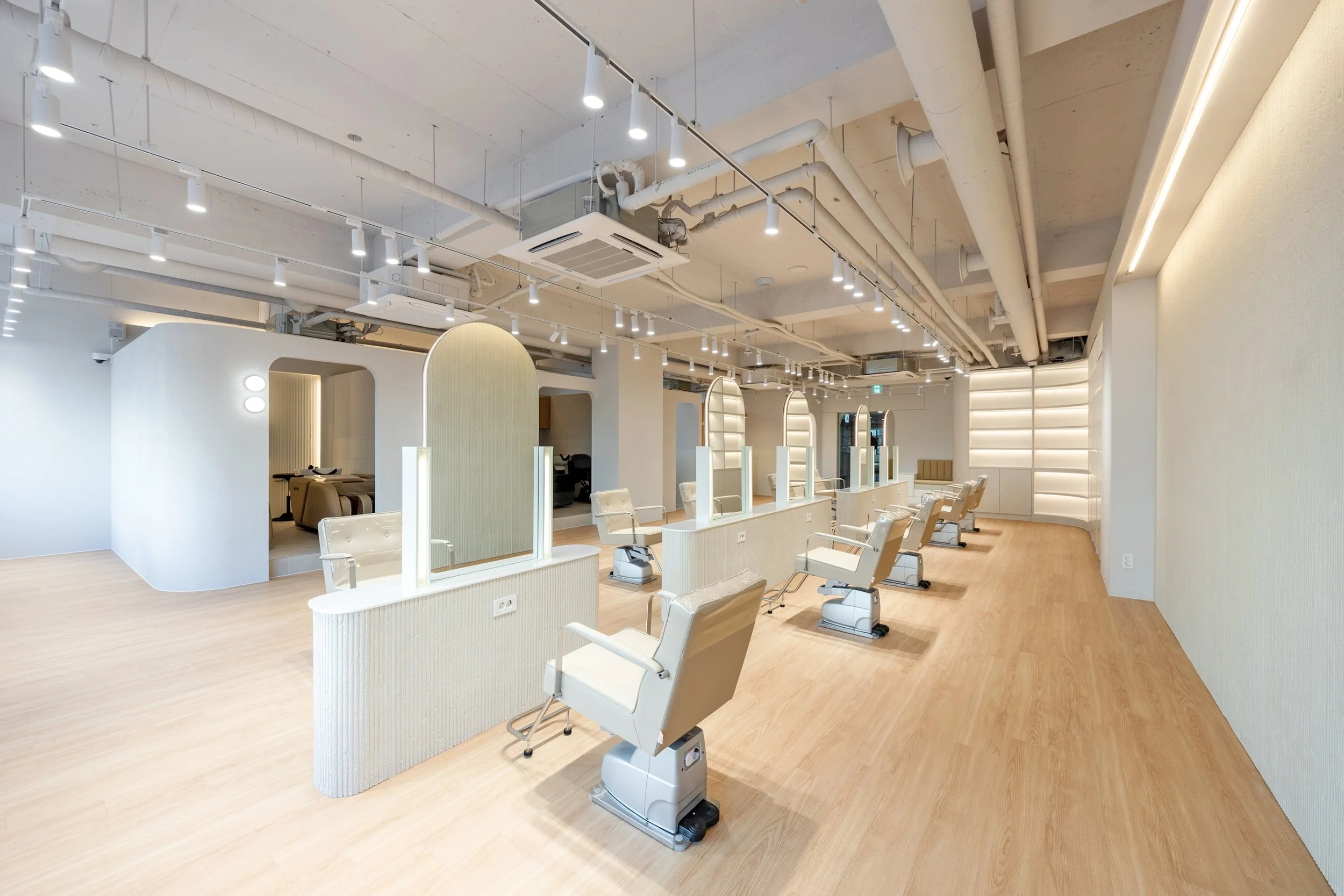 Empty salon with white chairs, mirrors, and light wood flooring.