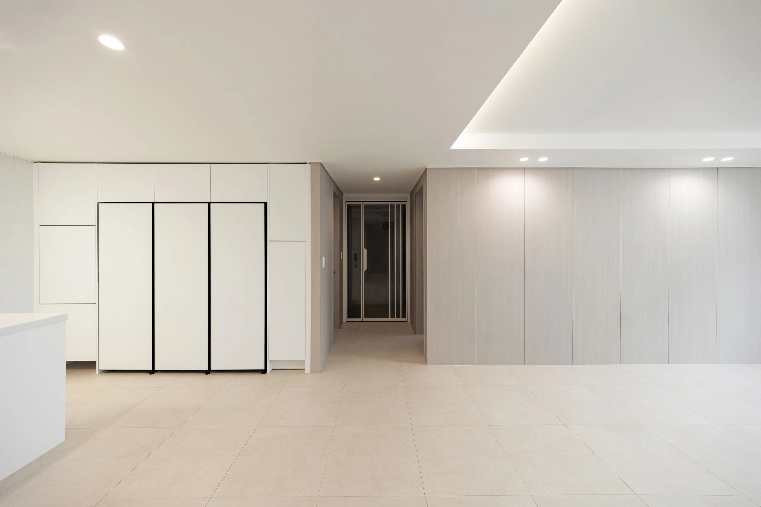 Minimalist modern interior with beige tiled floor, white and light wood walls, ceiling lights, and sliding elevator door.