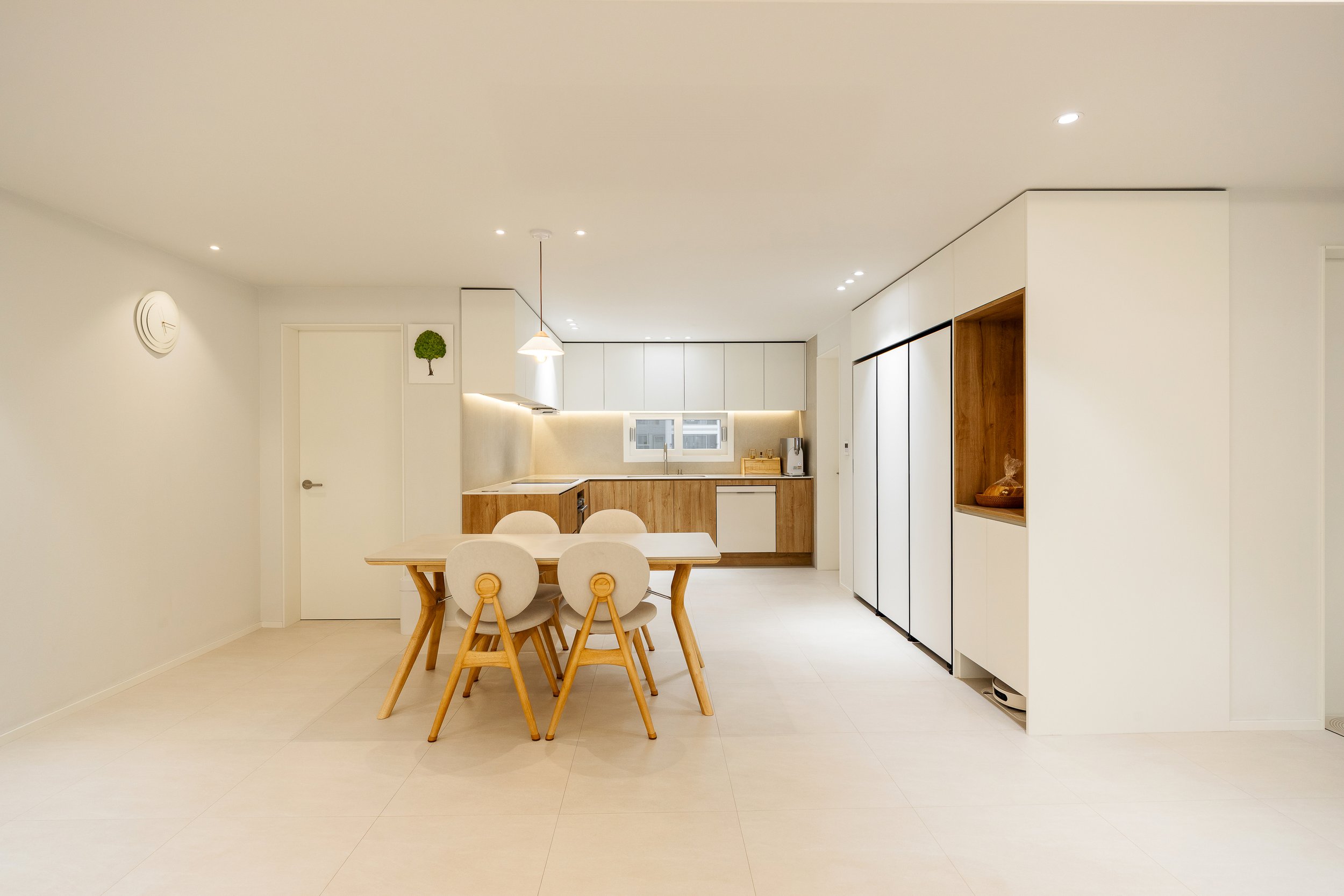 Minimalist kitchen and dining area with white walls, wooden accents, and a light-colored table with four chairs.
