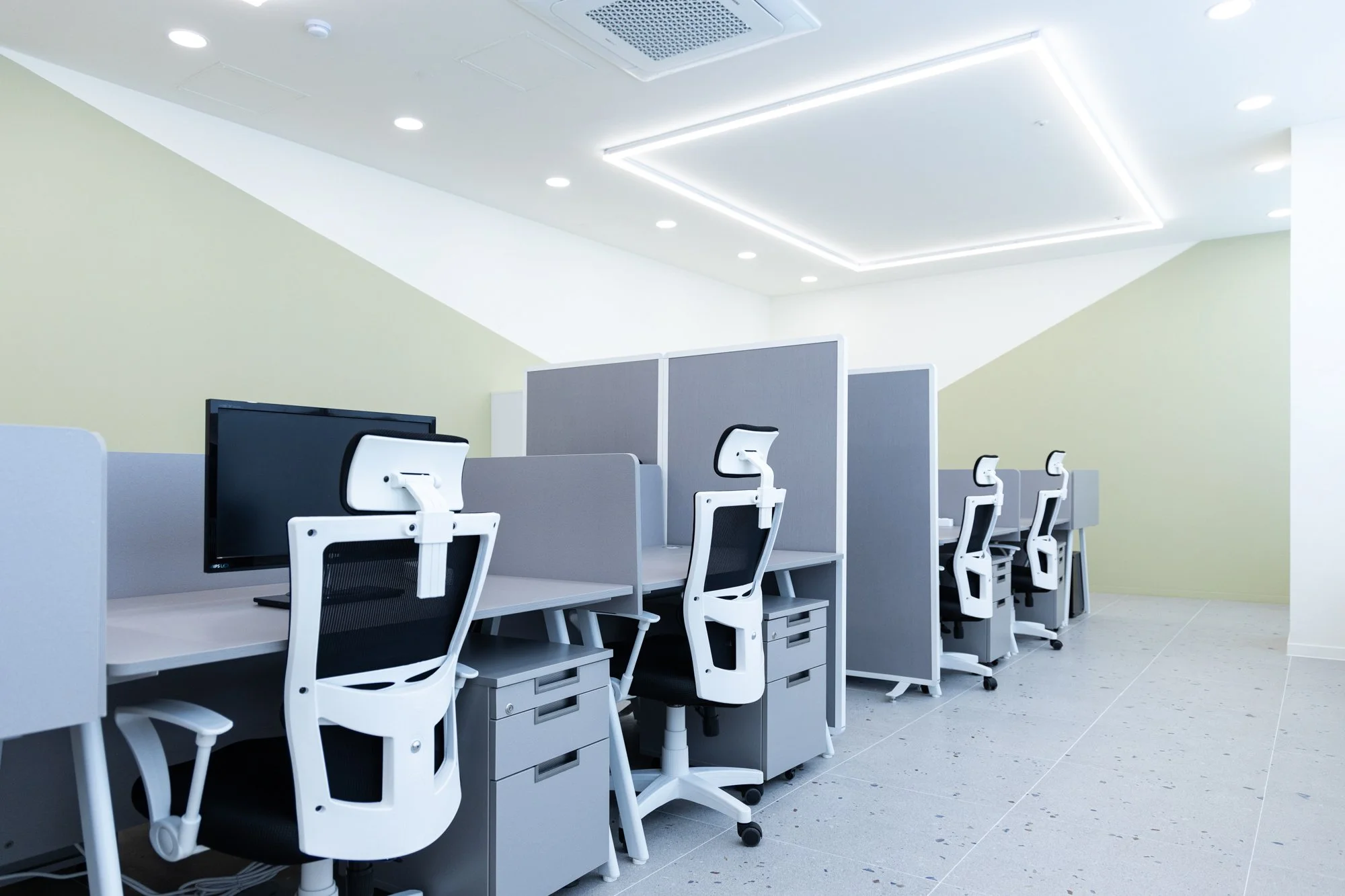 Empty modern office workspace with desks, ergonomic chairs, computers, and partitions under white ceiling with lighting.
