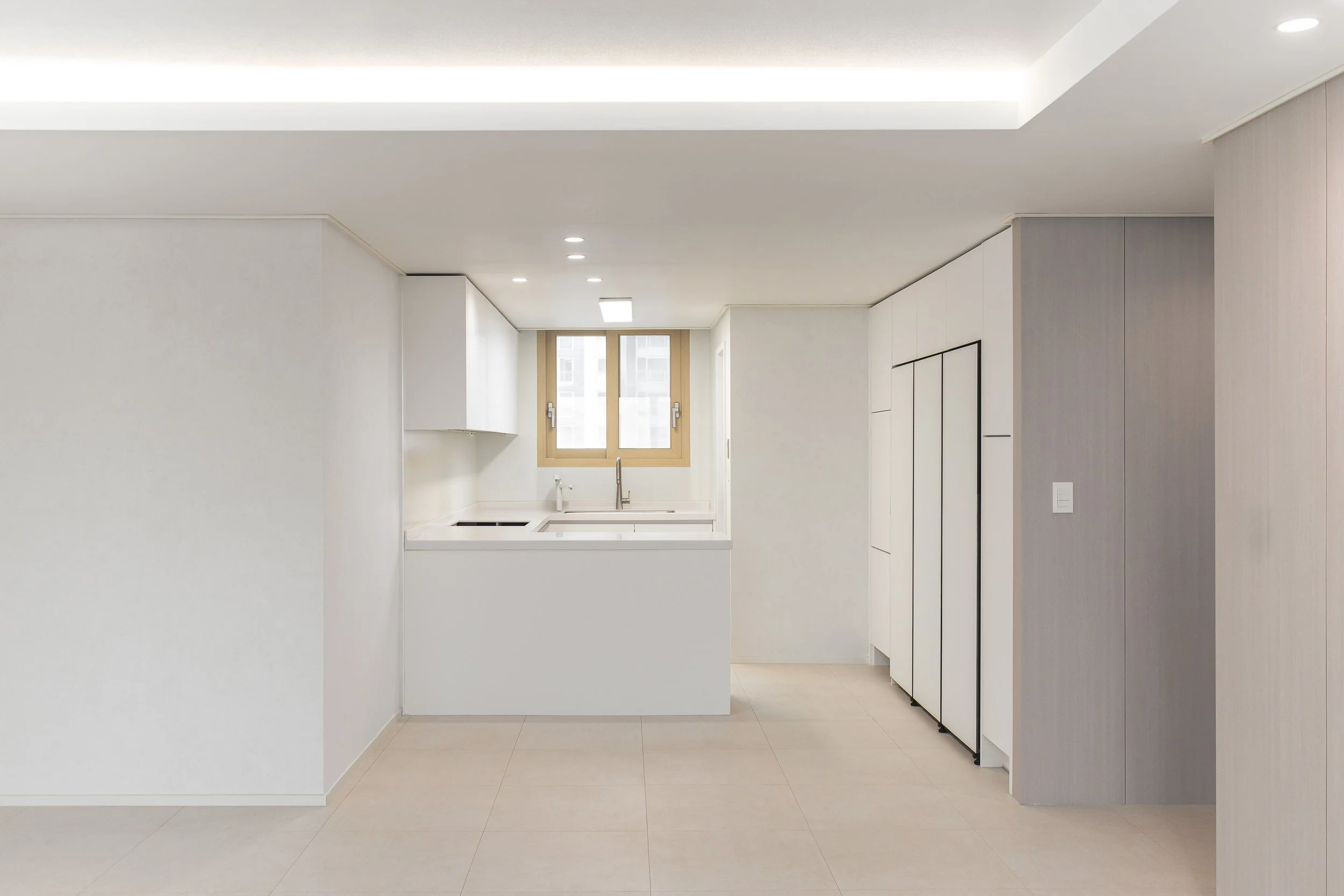 Minimalist white kitchen with a window over the sink, beige tiled floor, and simple cabinetry.