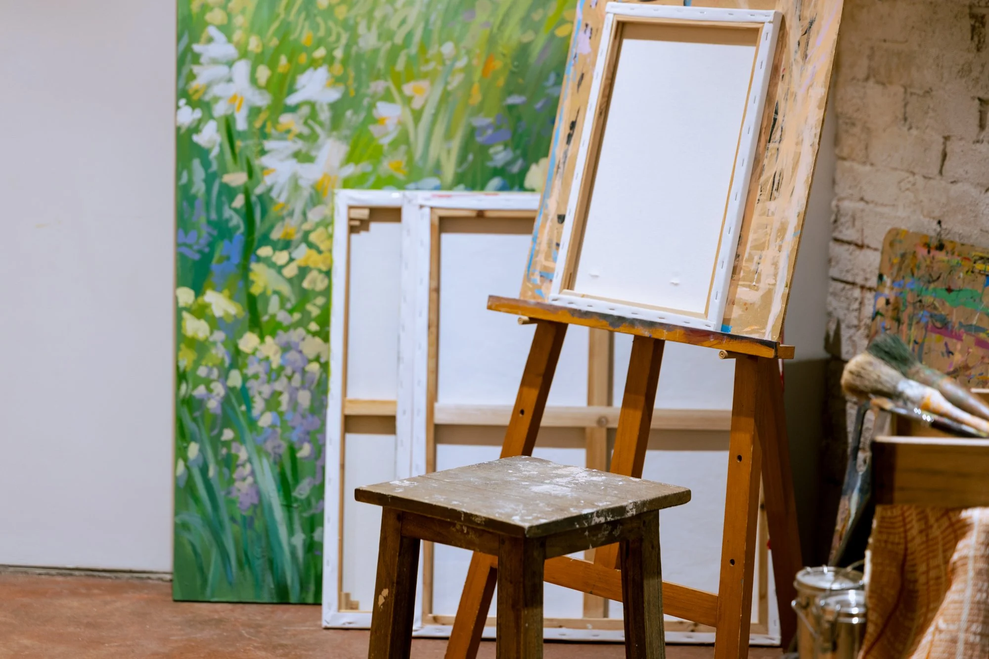 Art studio with blank canvases on easels, a small wooden stool, and a mural of flowers on the wall.