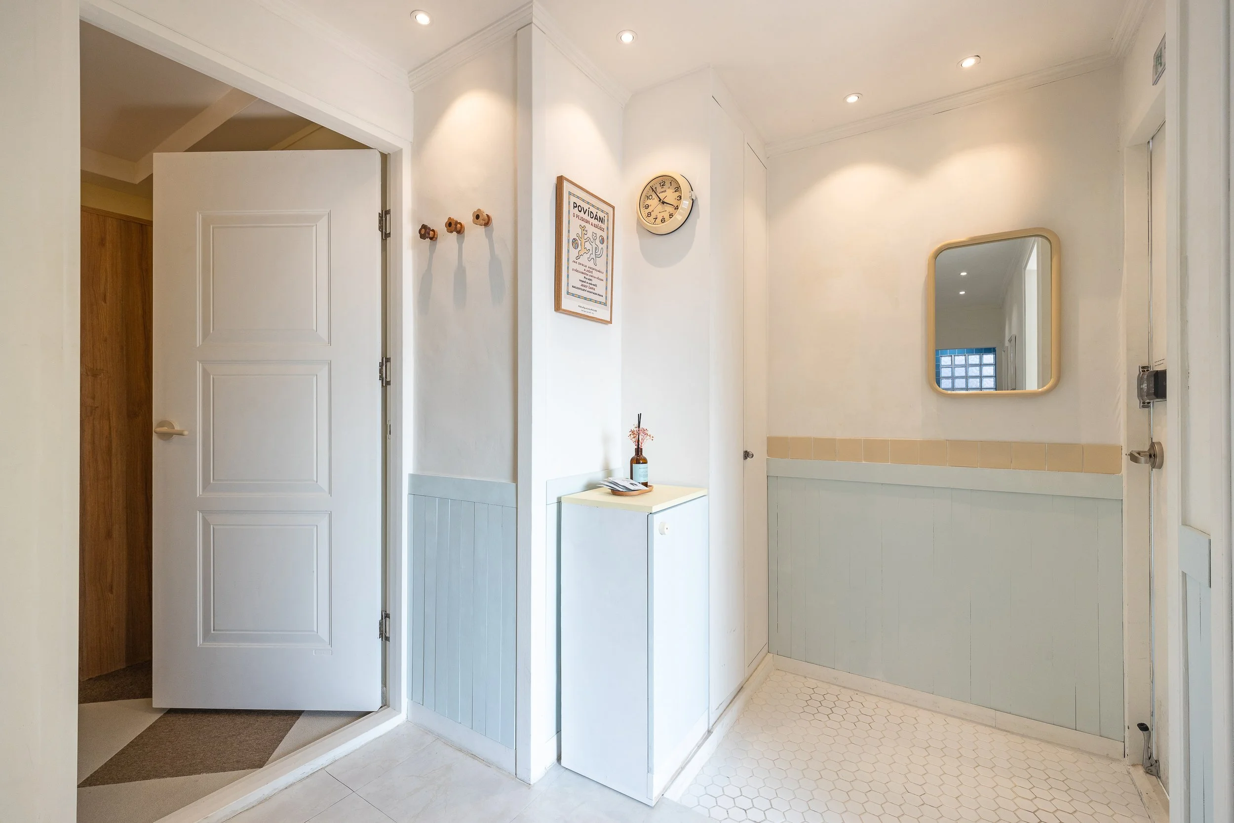 Entryway with open door, wall clock, mirror, hooks, and small table with decorative items