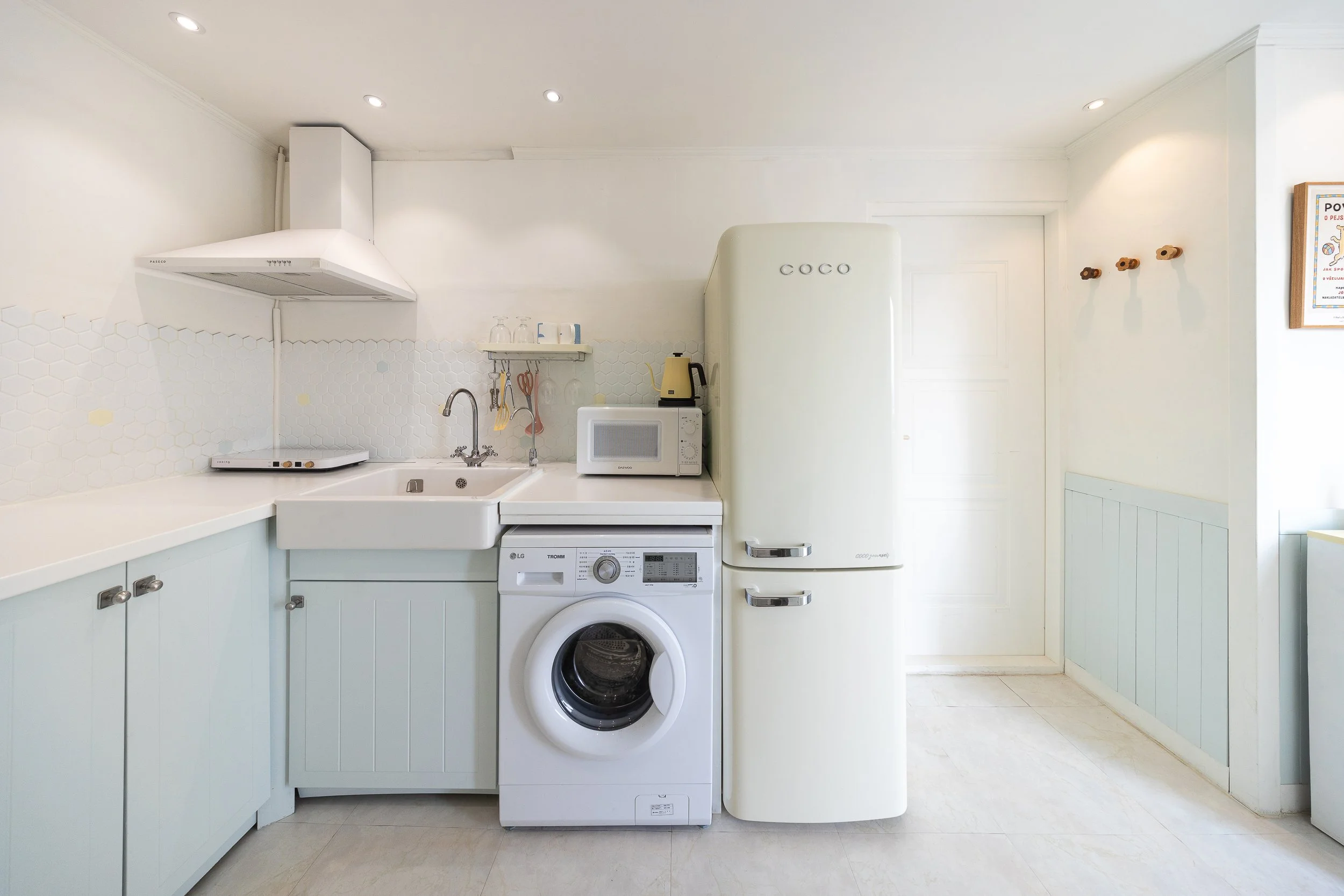 Bright, minimalist kitchen with white cabinets, a white oven, microwave, and vintage-style refrigerator, light wood flooring, and a white hexagon tile backsplash.
