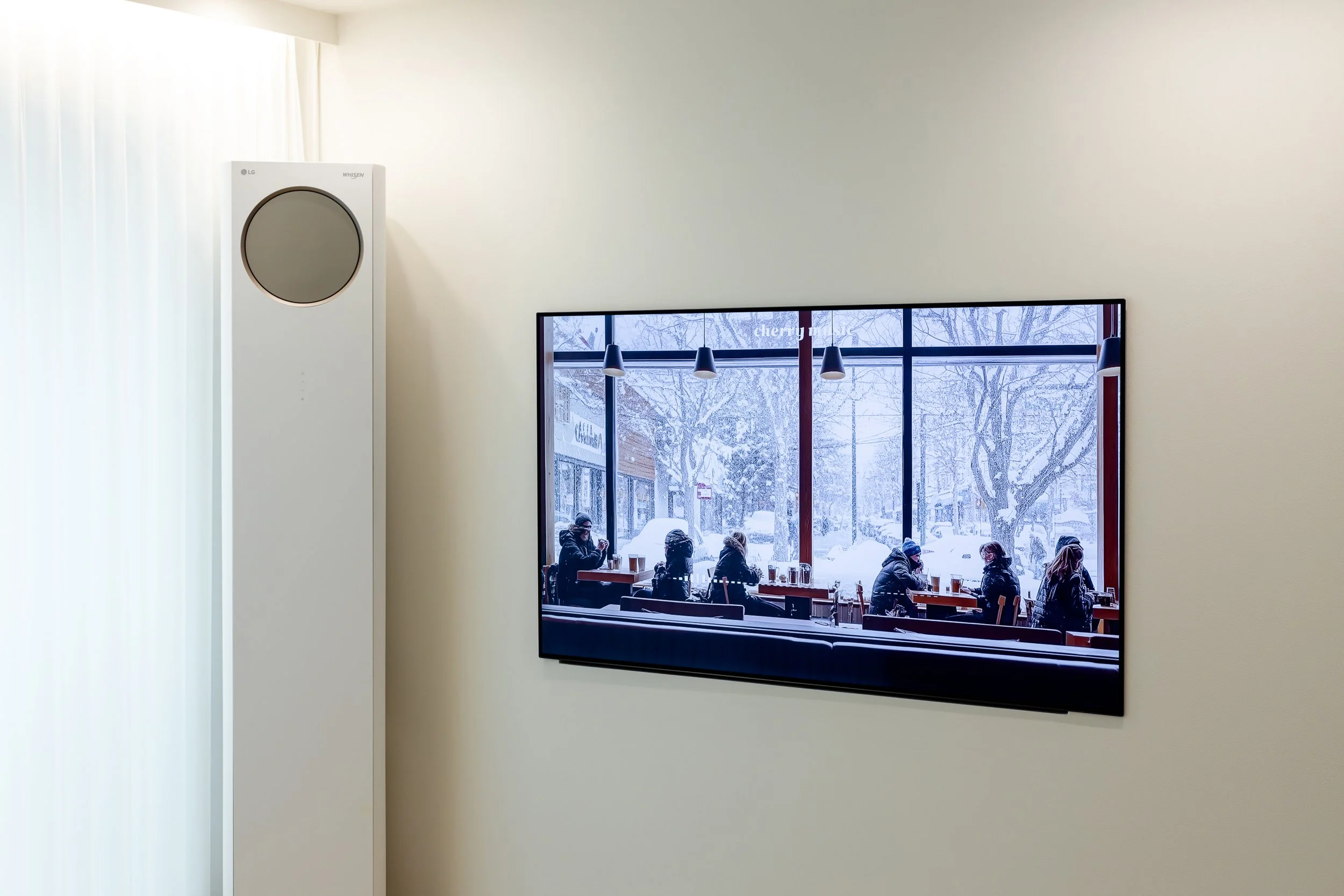 A television mounted on a beige wall shows a snowy winter scene outside a cafe with customers sitting at tables.