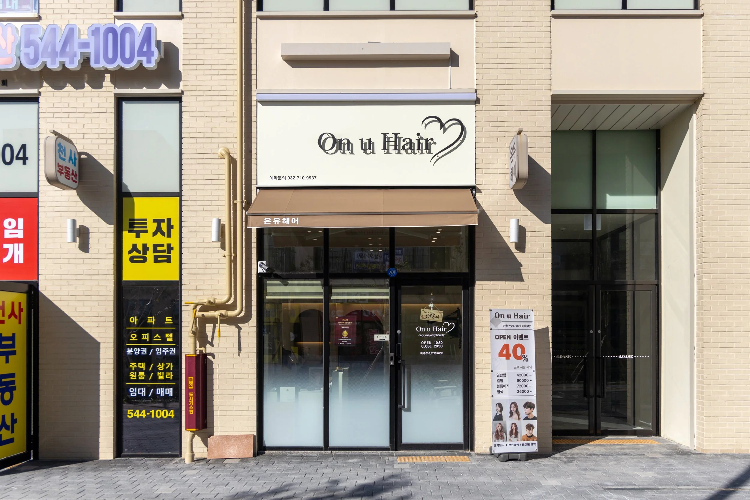 Exterior front of a hair salon named 'On u Hair' with glass doors, white sign with black text, and a promotional signboard outside advertising a 40% discount.