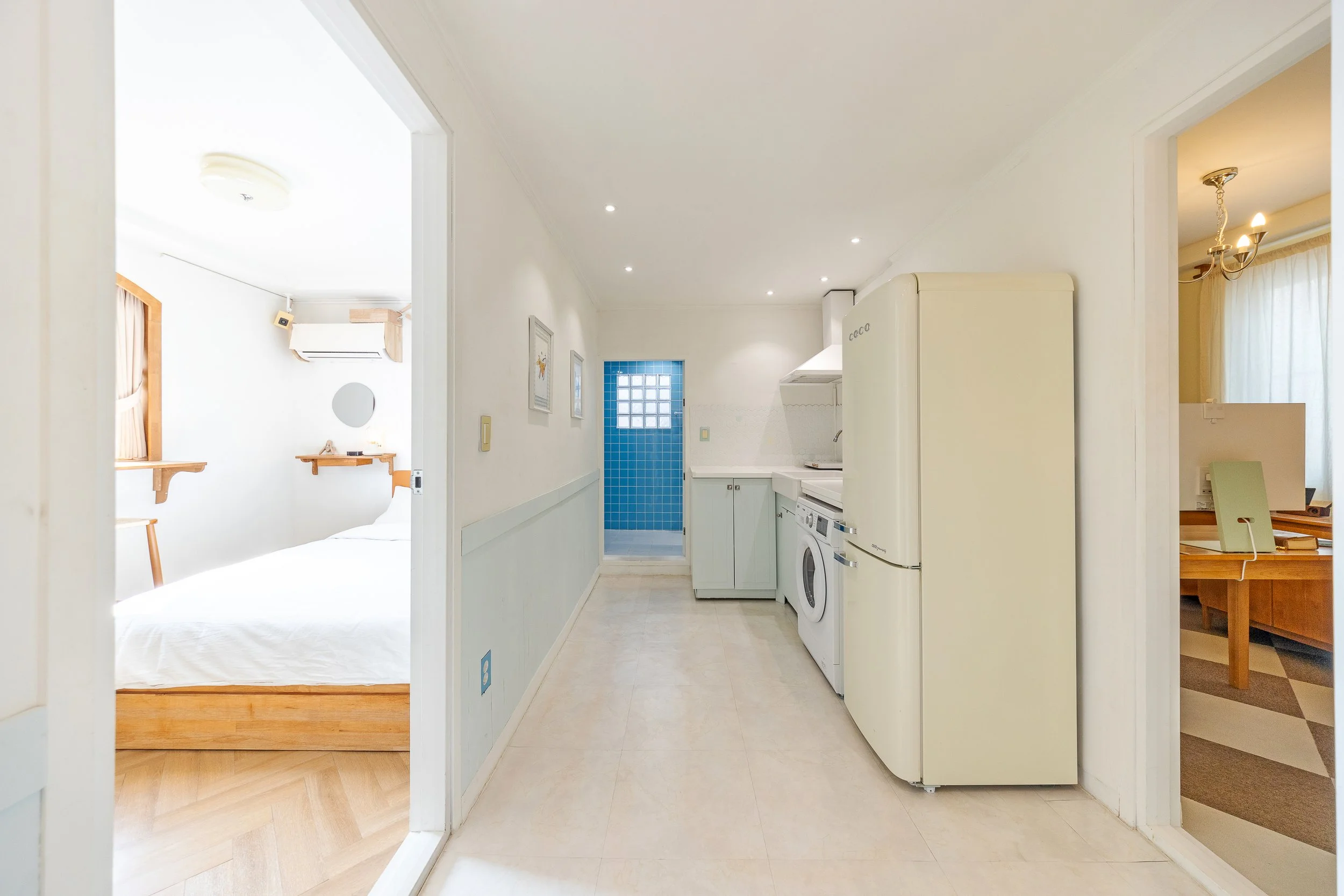A small kitchen with a white refrigerator, washing machine, and green cabinetry, with two bedrooms visible on either side.