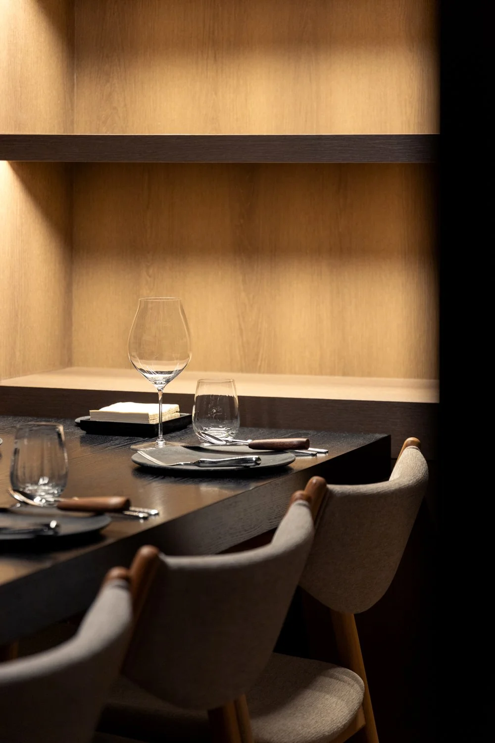 Empty dining table set with plates, glasses, silverware, and napkins in a modern restaurant with wooden décor.
