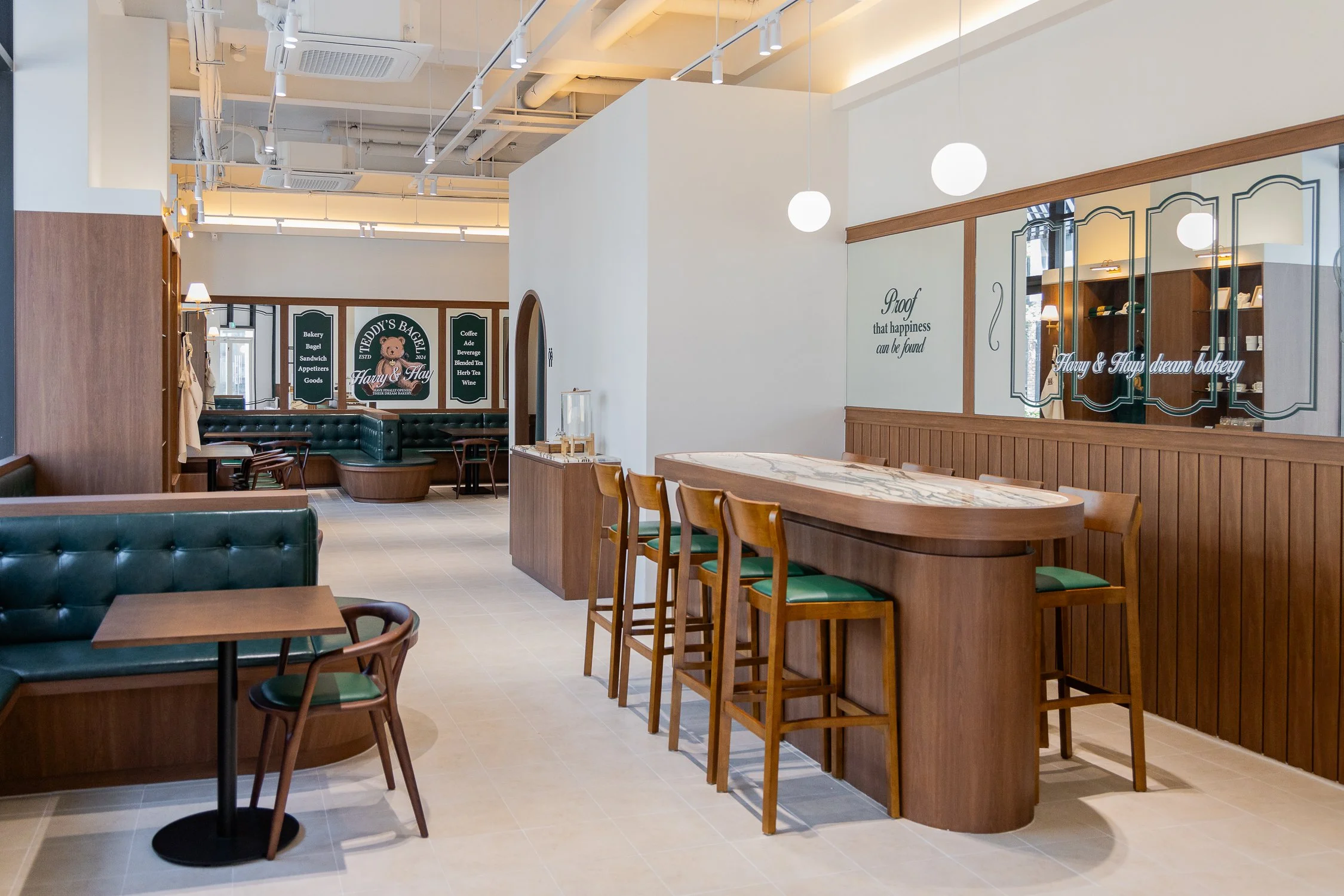Empty bakery or café interior with wooden furniture, green cushioned seating, and decorative mirrors, with signs on the walls.