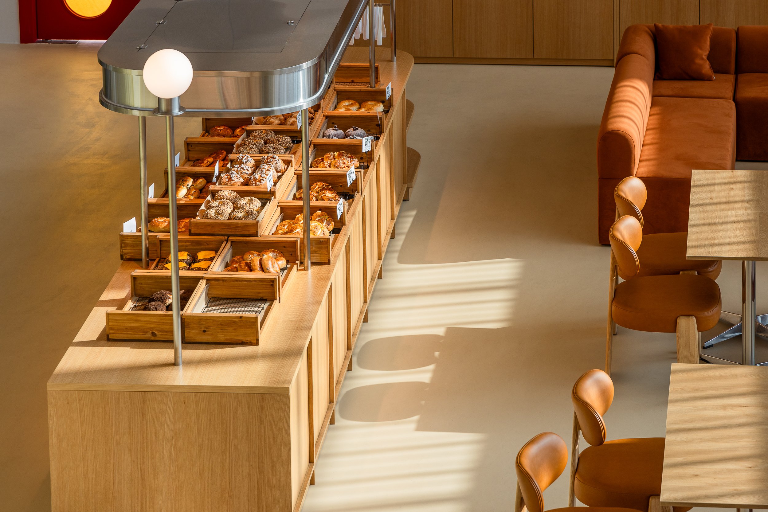 Bakery display with assorted bread and pastries on a wooden counter, in a cozy cafe setting with tables and chairs.