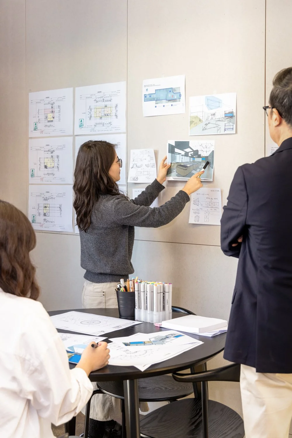 Group of architects discussing building design plans displayed on a wall during a meeting.