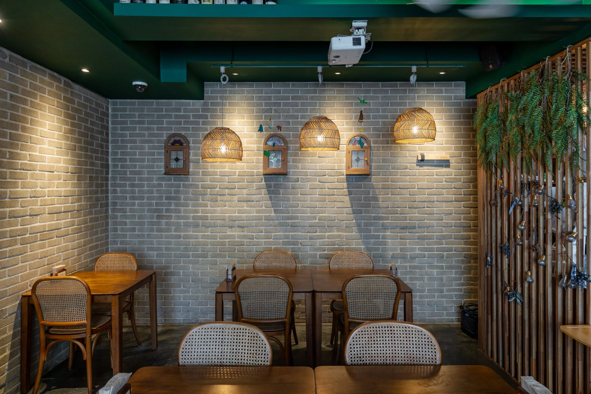 Interior of a cozy restaurant with brick walls, wicker pendant lighting, wooden tables and chairs, and decorative wall hangings.