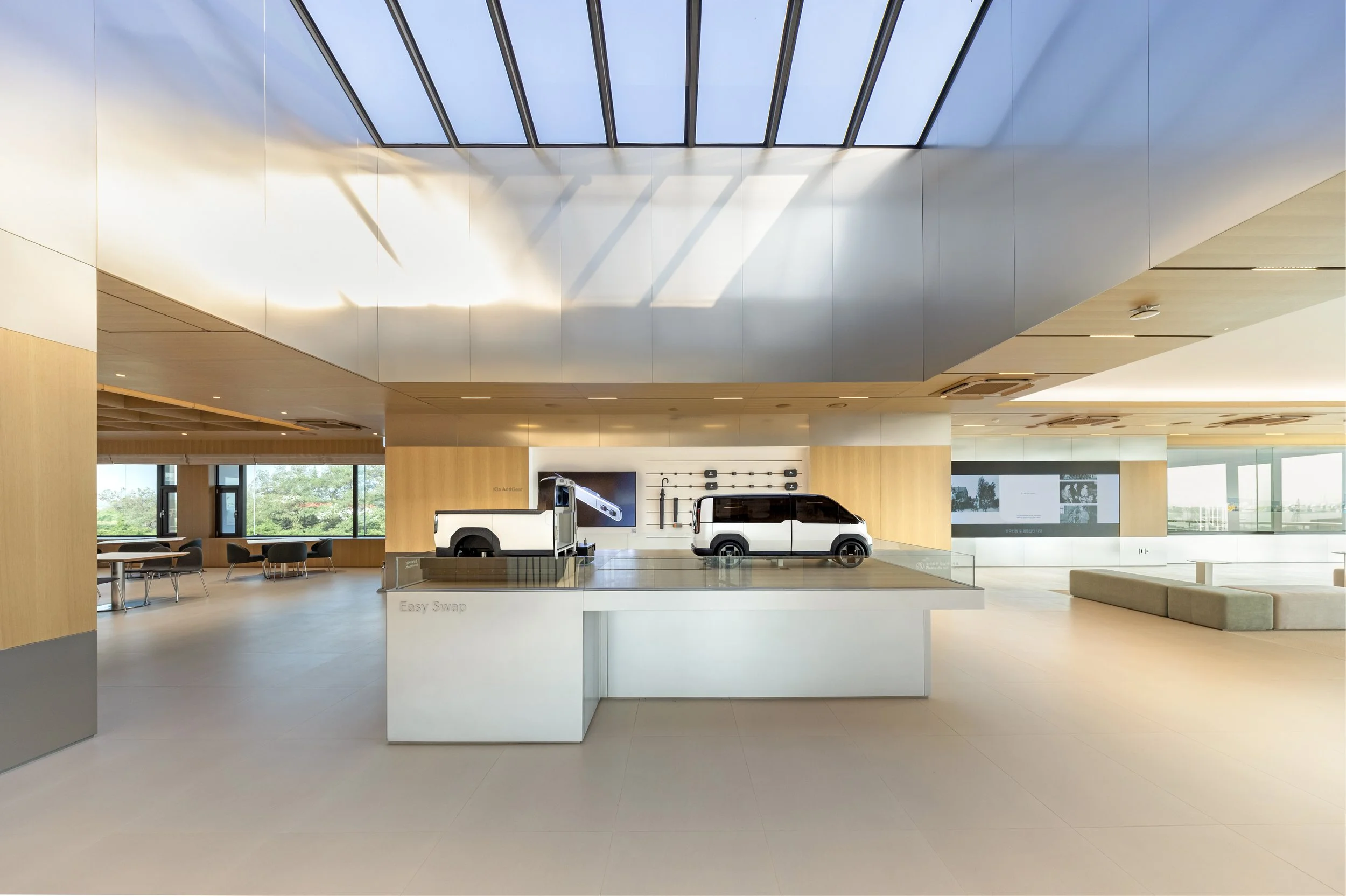 Modern showroom with a car customization display, including a white pickup truck model and vehicle parts, in a spacious, well-lit area with large windows and minimalist decor.