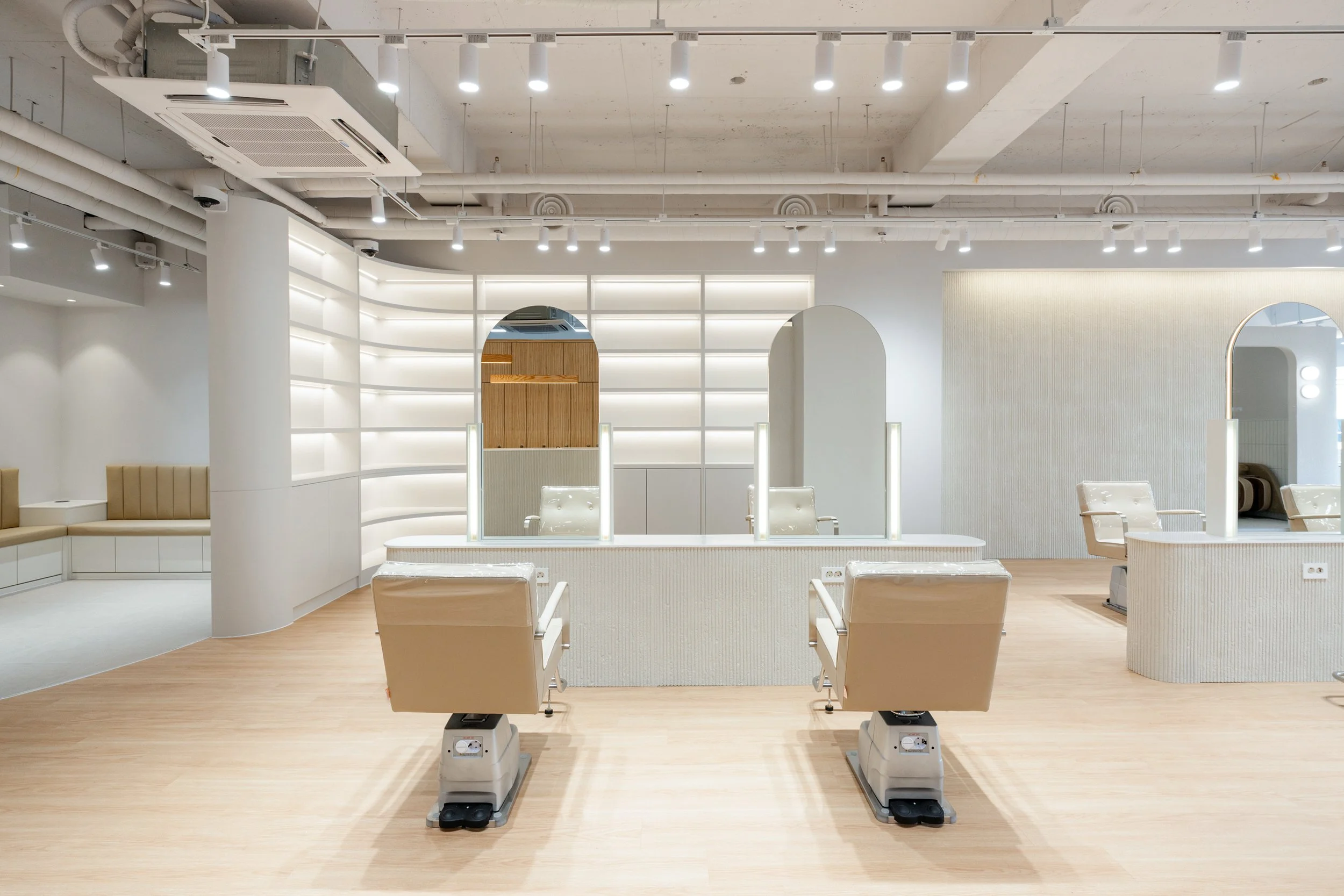 Empty modern salon with beige chairs, mirrors, and light wood flooring.