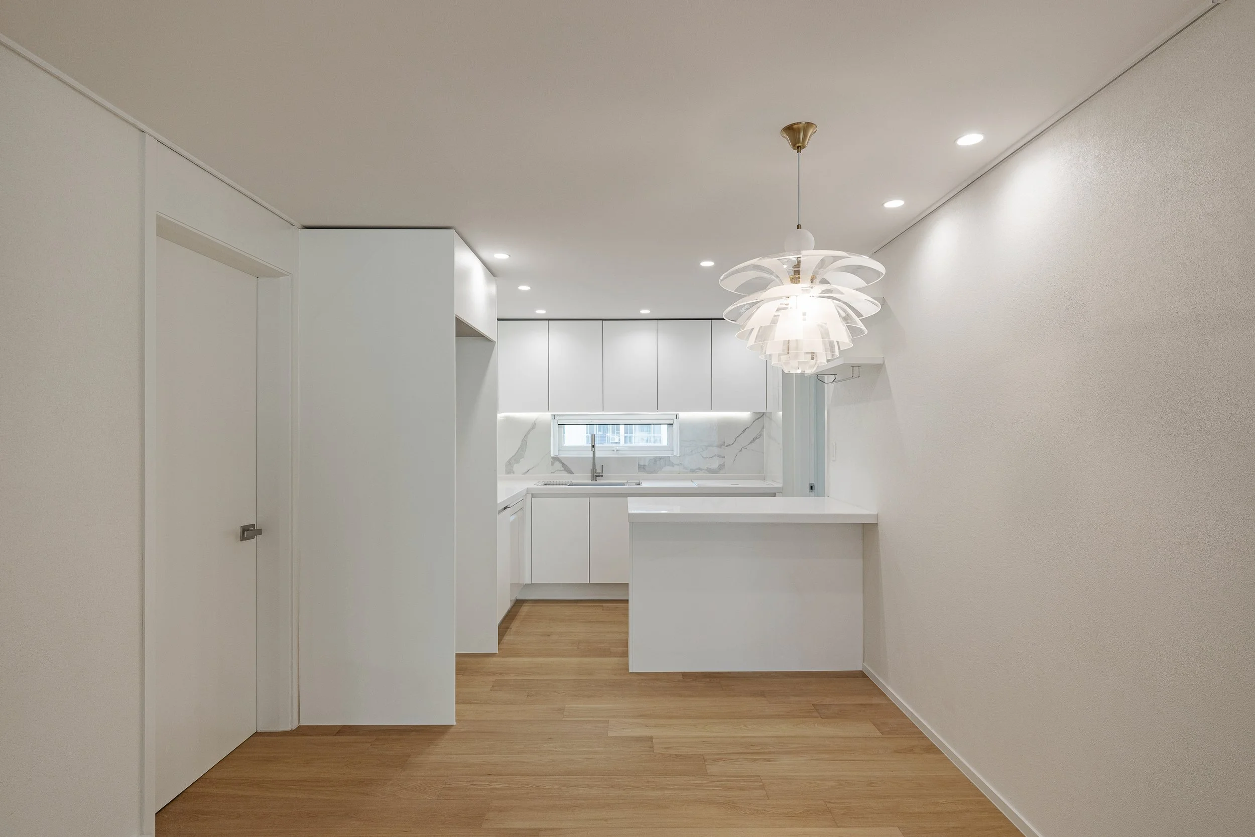 Freshly renovated kitchen with white cabinetry, marble backsplash, wooden flooring, and modern pendant lighting.