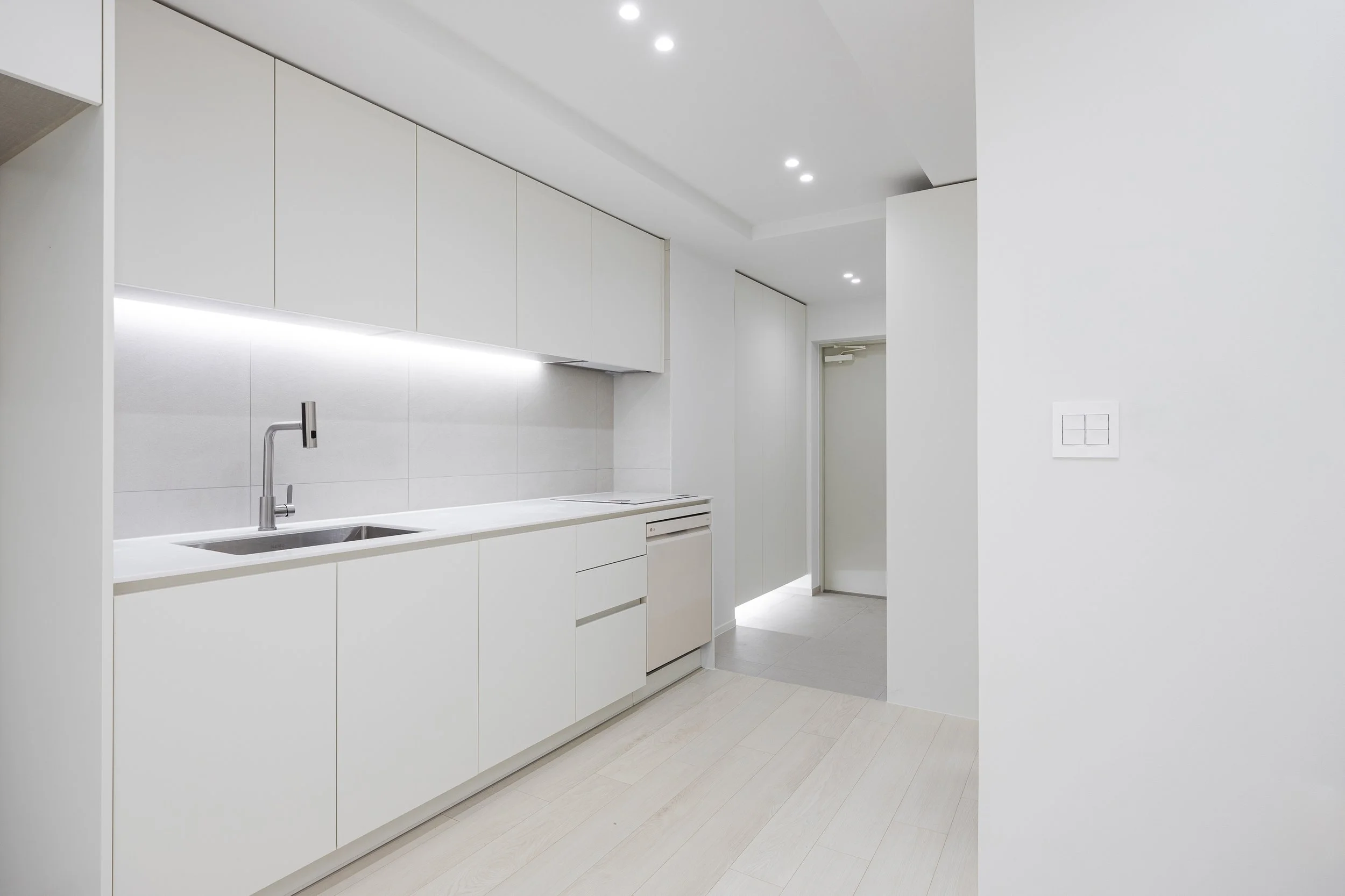 Minimalist white kitchen with sleek cabinets, a sink, and under-cabinet lighting in a modern home.