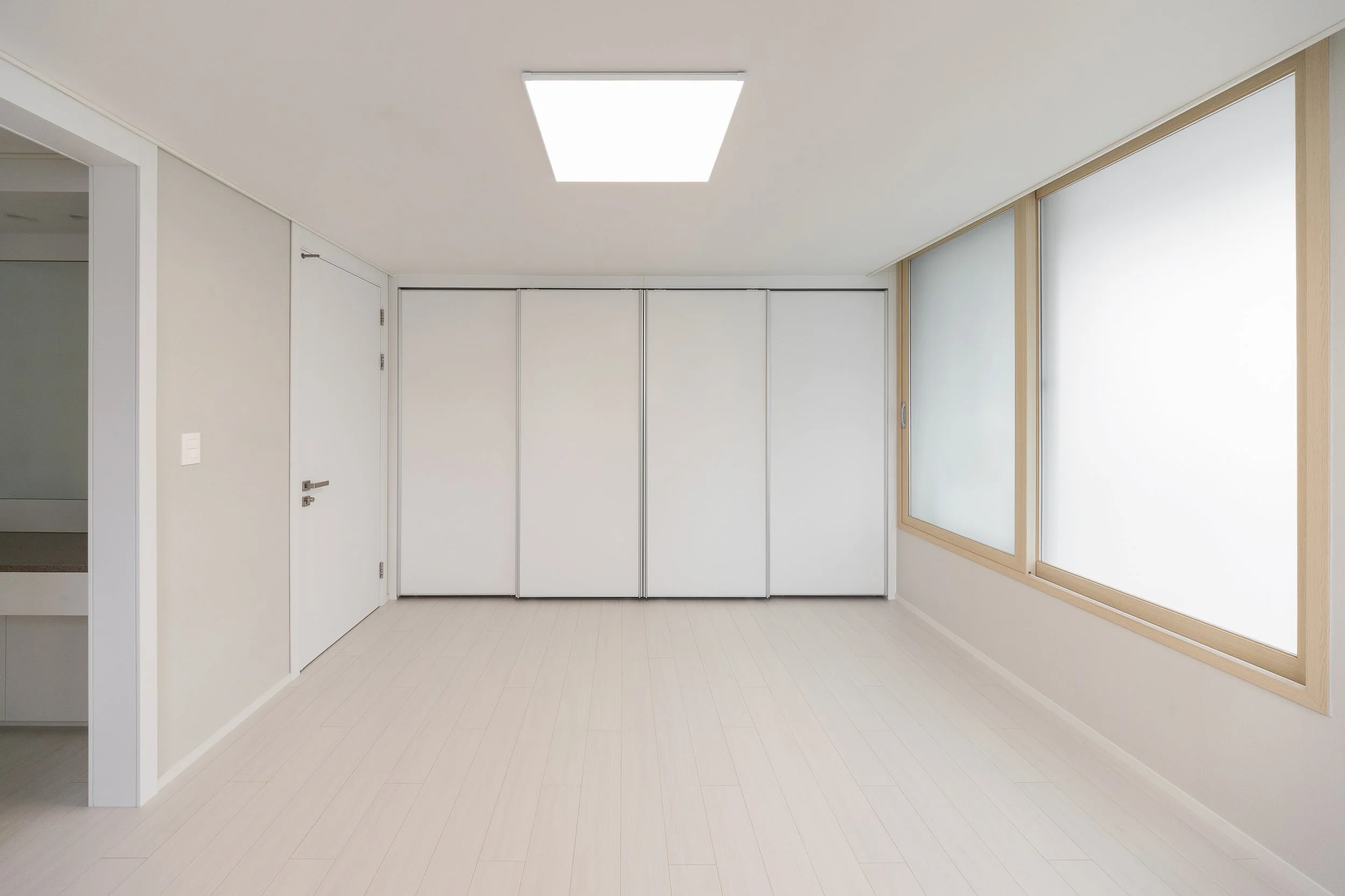 Empty room with beige walls, white ceiling, light wood flooring, two large frosted windows, and a white closet with sliding doors.