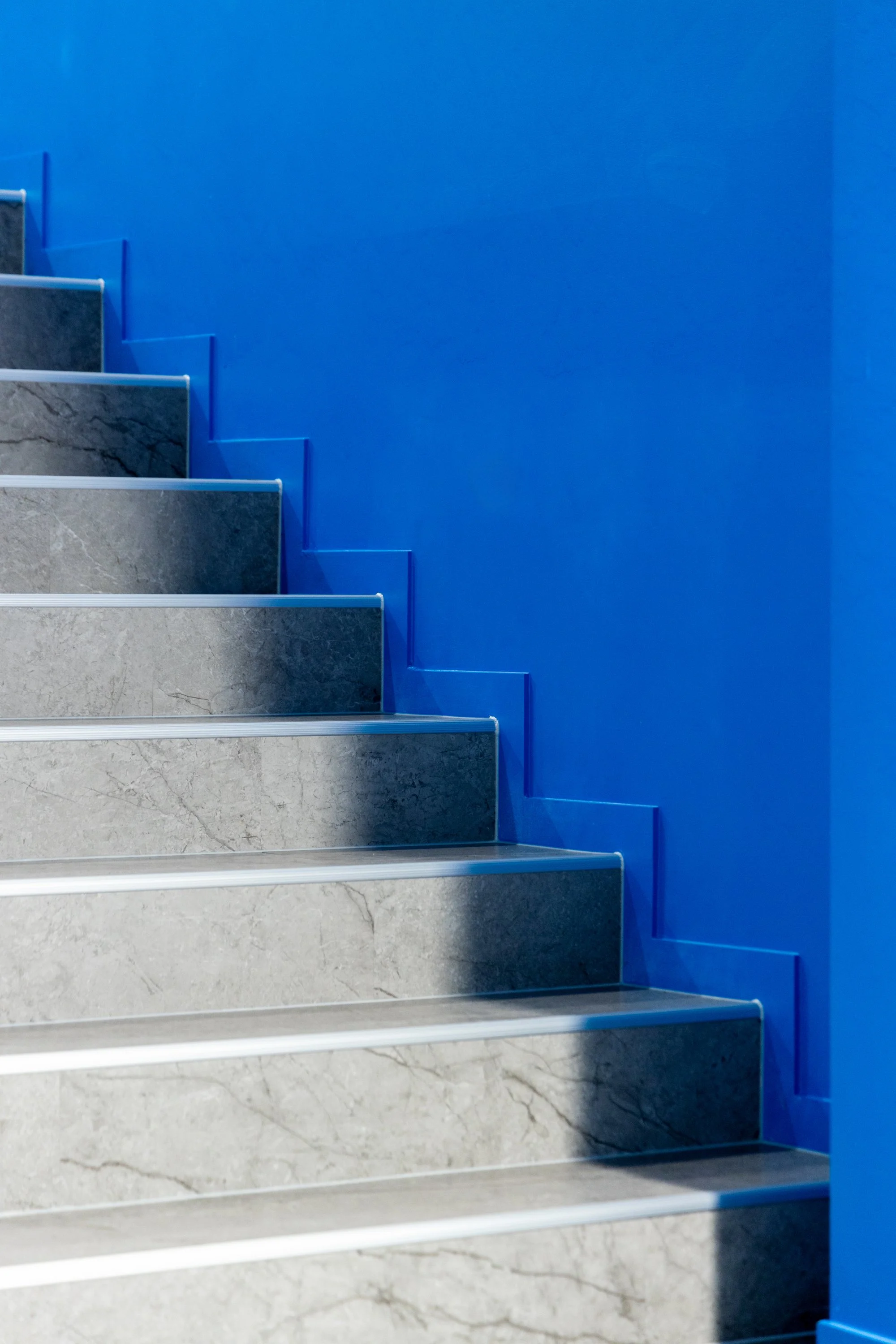 Interior staircase with gray marble steps, silver edges, and a blue wall on the right side.
