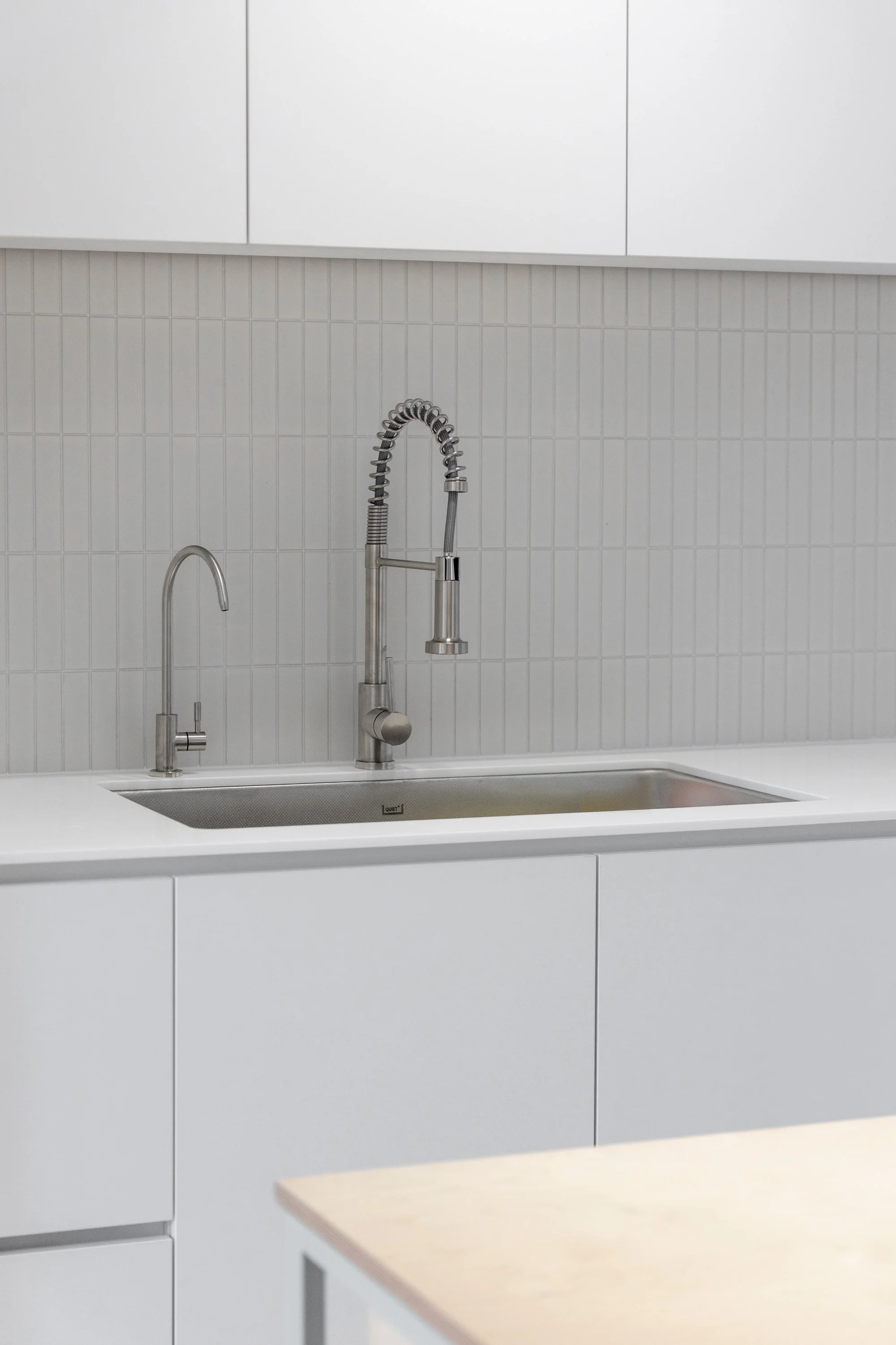 Empty kitchen sink with two modern silver faucets and a beige countertop in a minimalistic kitchen
