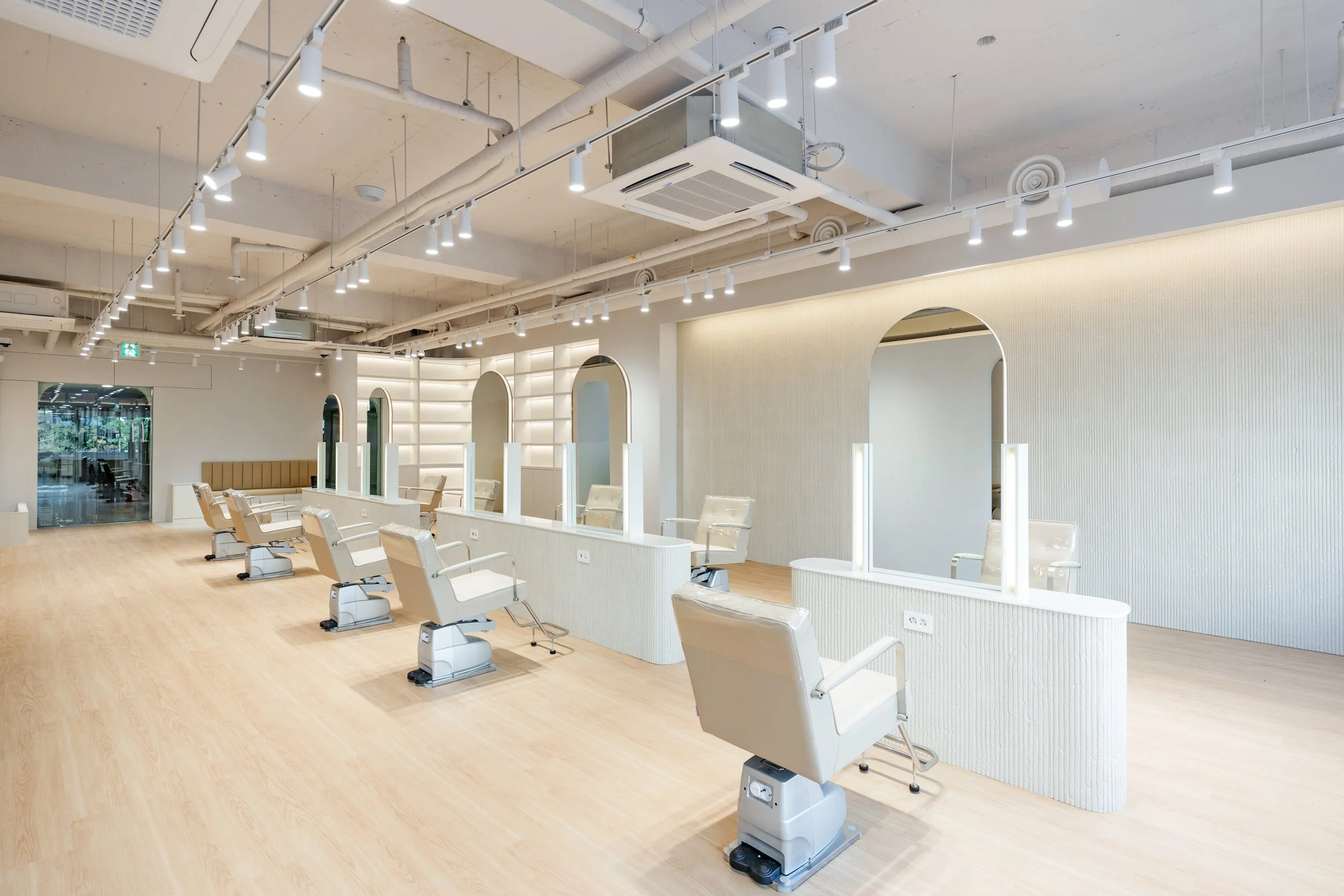 Empty hair salon with white chairs and mirrors, bright lighting, light wood flooring, and a modern minimalist design.