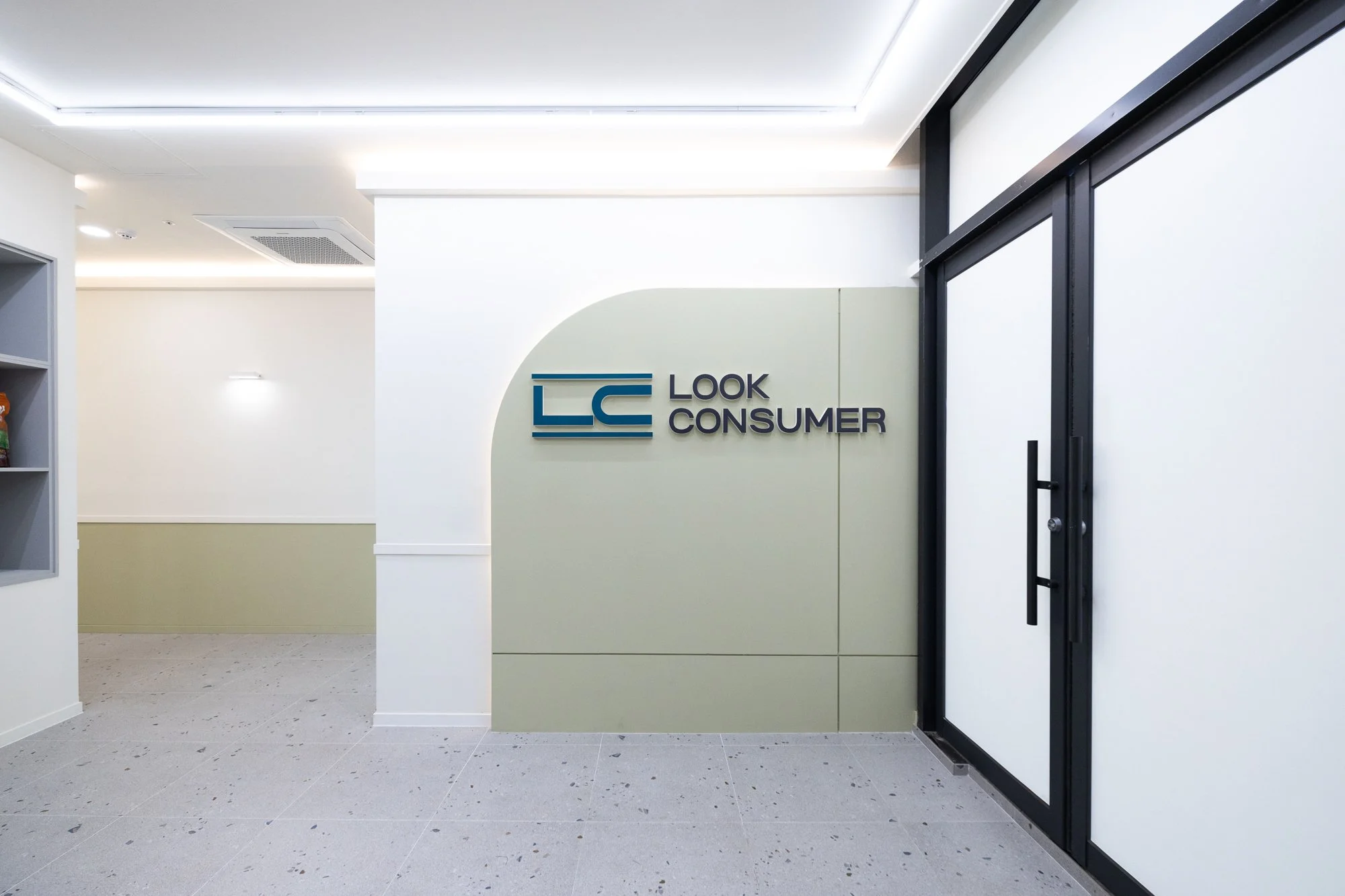Interior of a modern office or clinic with the sign 'Look Consumer' on the wall near black-framed glass doors.