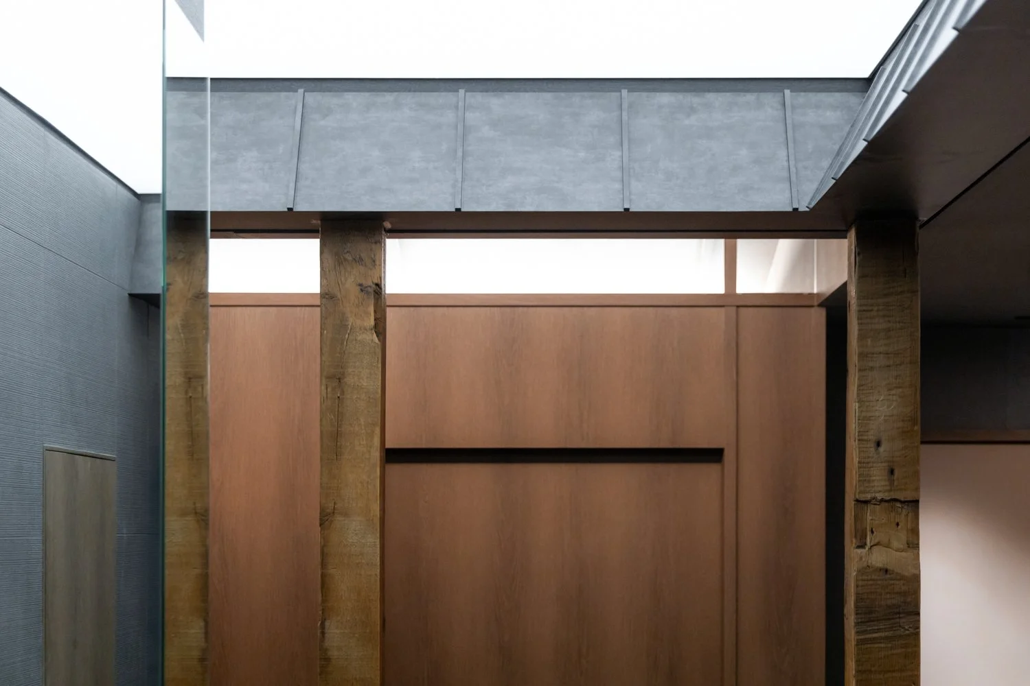 Interior view of a modern building with wooden and concrete architectural elements, including vertical wooden beams and high ceiling with skylight.