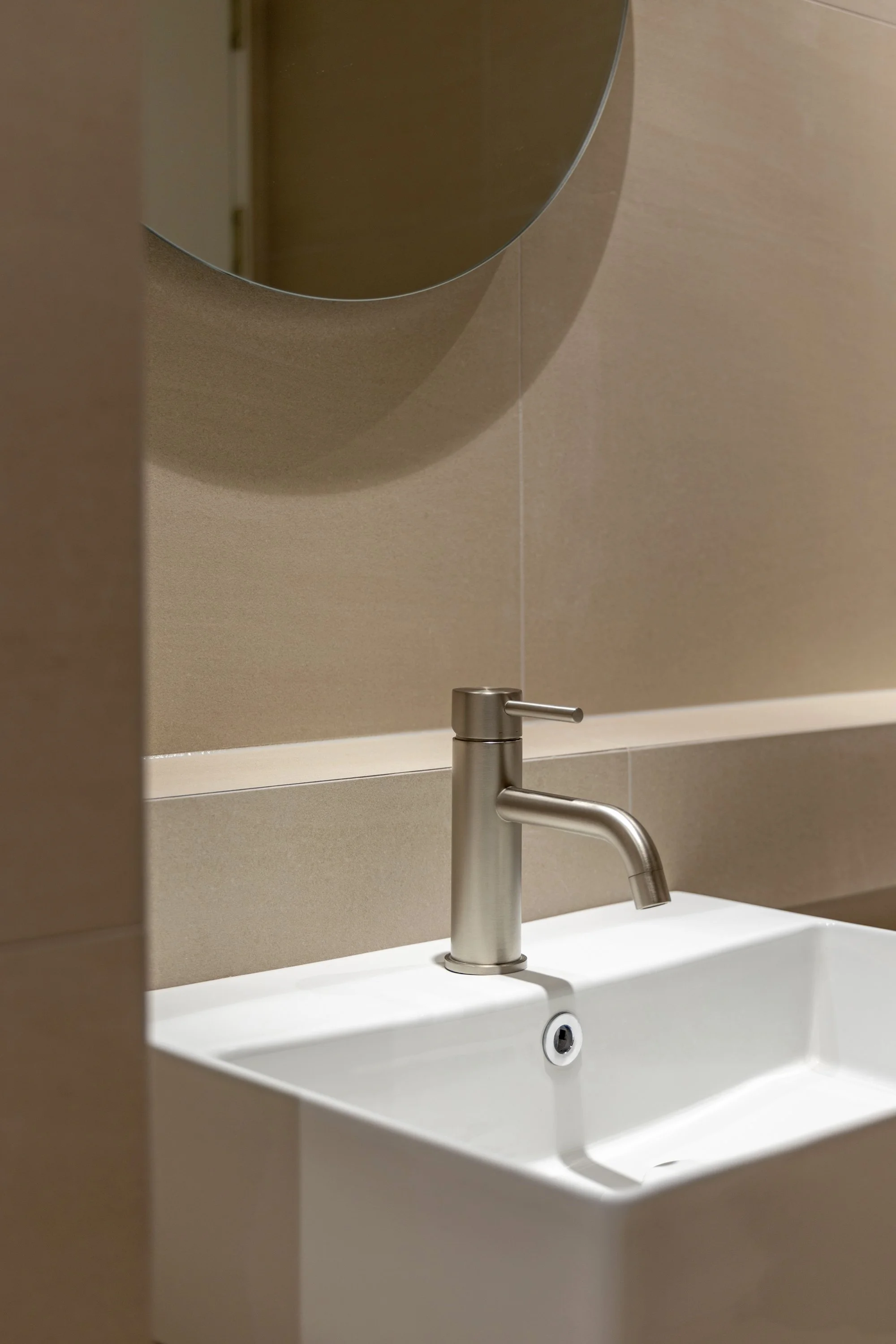 A bathroom sink with a modern stainless steel faucet and a small mirror above it.