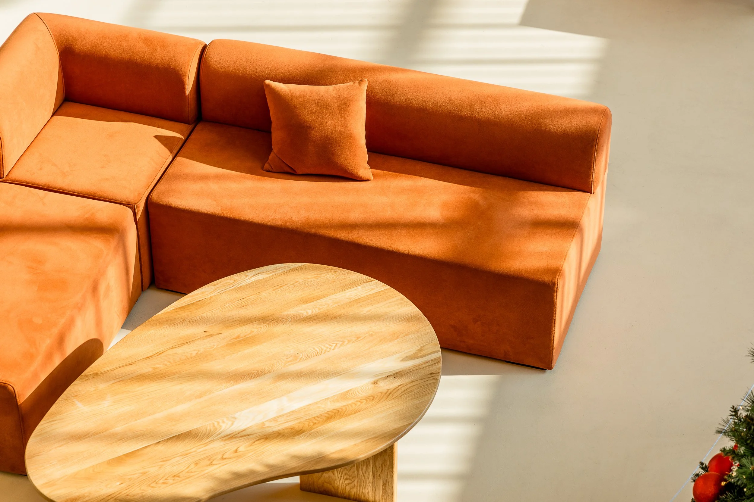 An orange sectional sofa with a matching pillow and a wooden oval coffee table in a bright room.
