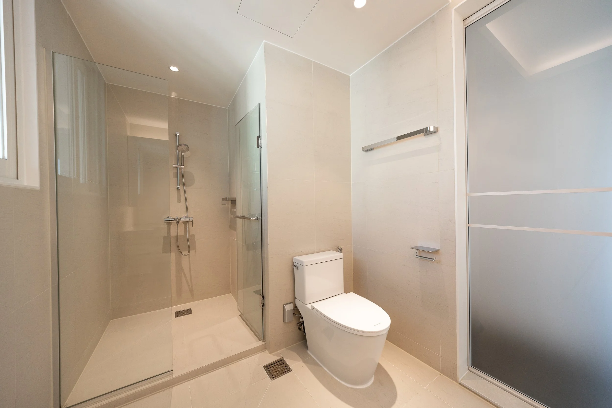 Modern bathroom featuring a walk-in shower with glass door, a toilet, frosted sliding door, and minimalistic fixtures.