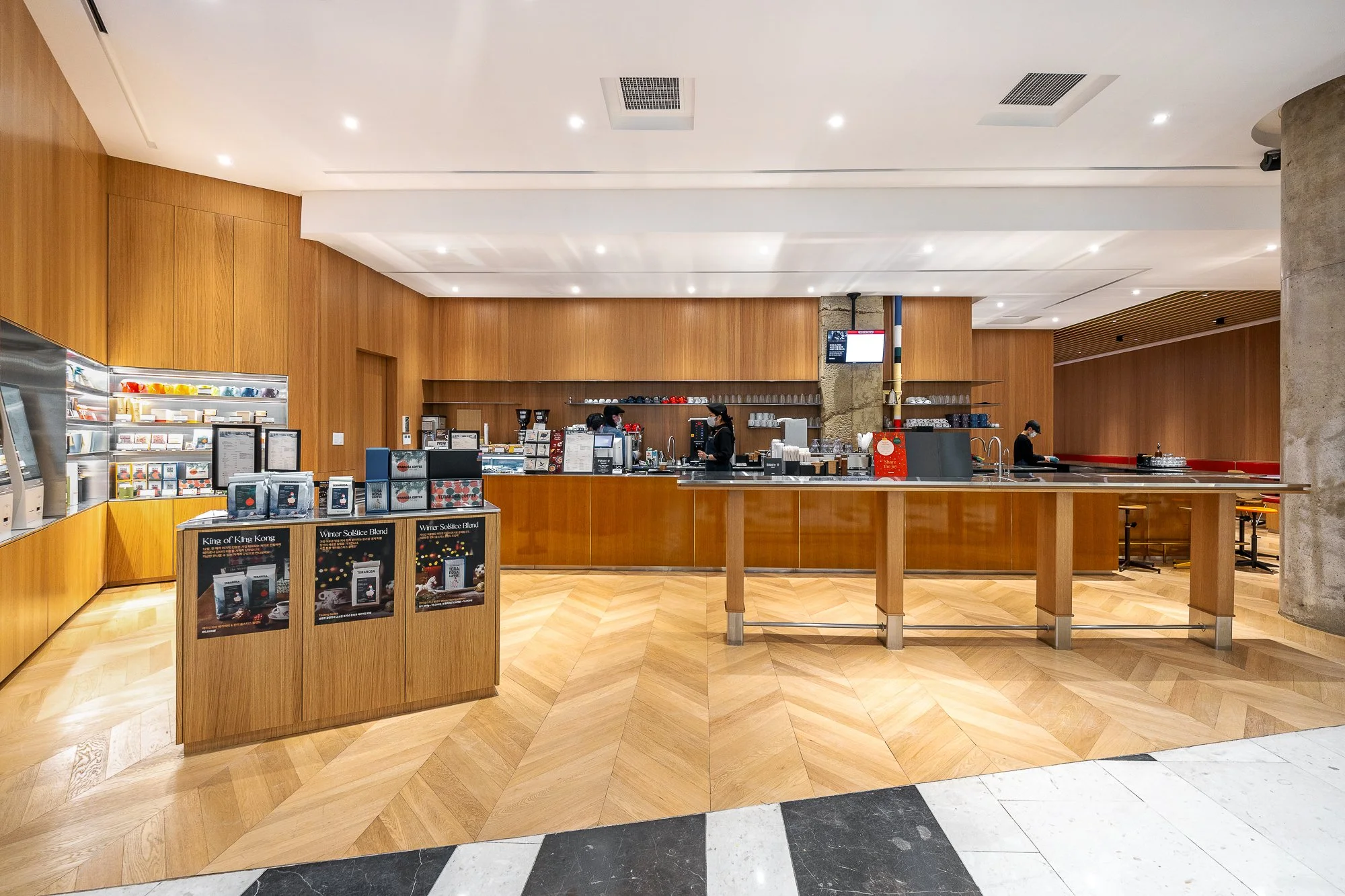 Modern coffee shop with a wooden interior, counter area with staff, and promotional display for holiday-themed products.