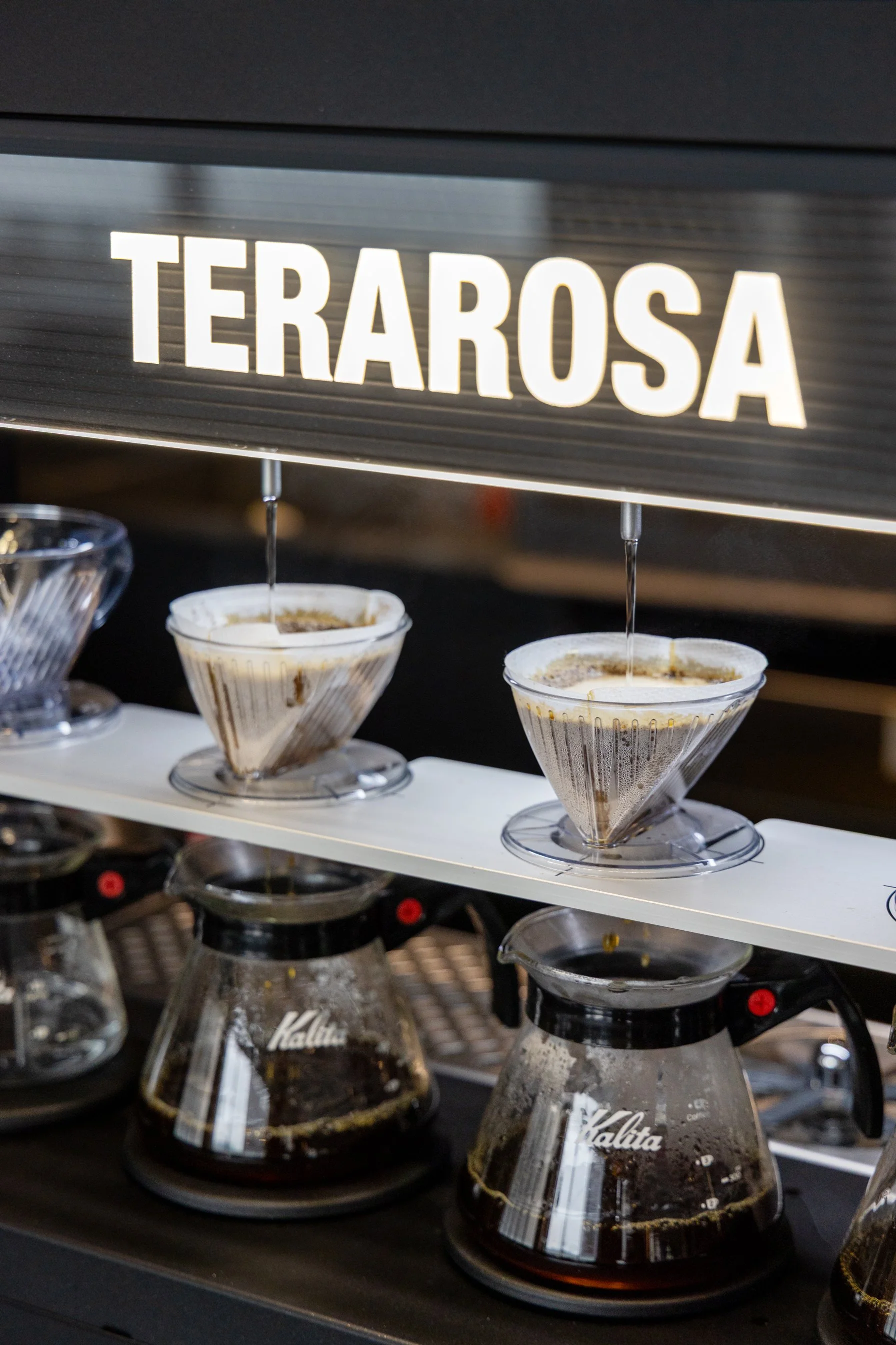 Pour-over coffee brewing setup with coffee drippers and glass carafes, labeled 'Terarosa'.