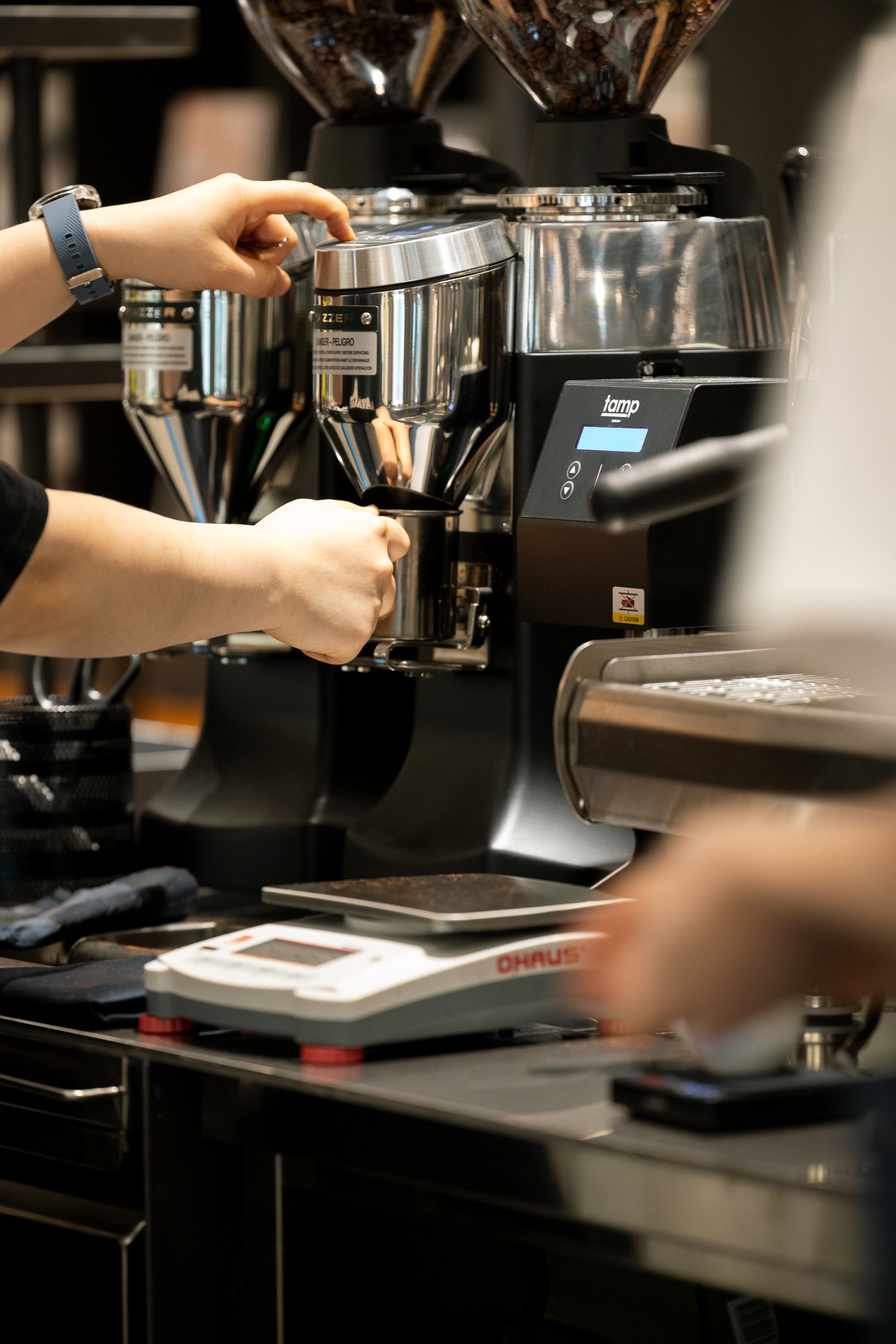 Barista preparing coffee at an espresso machine with a digital scale on the countertop.